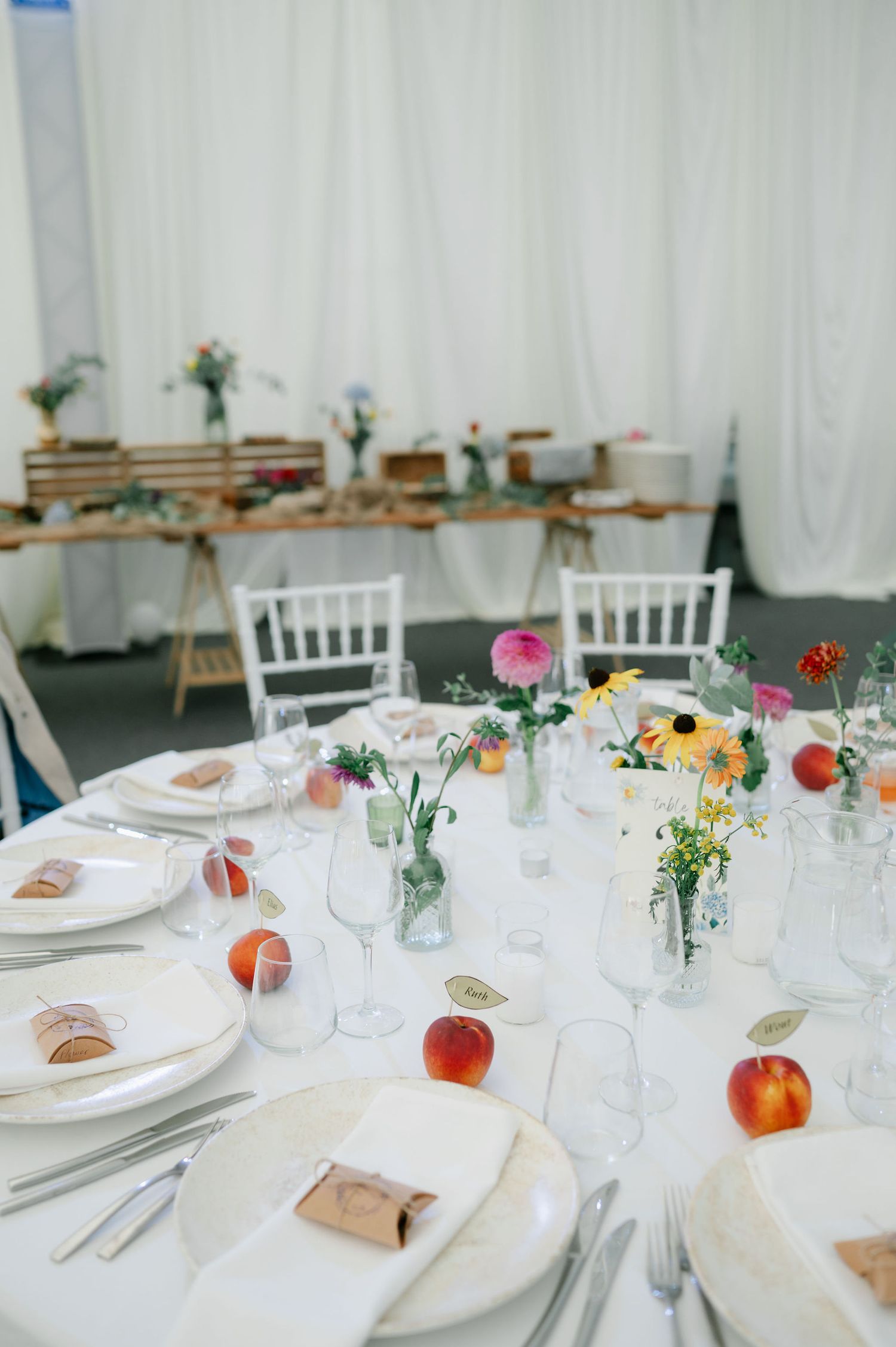 Long view of wedding reception tables with white place settings and colorful floral centerpieces.