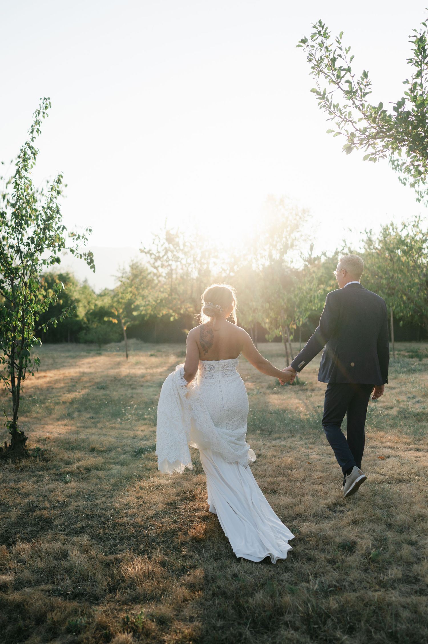 Sunset wedding photos with couple running through orchard.