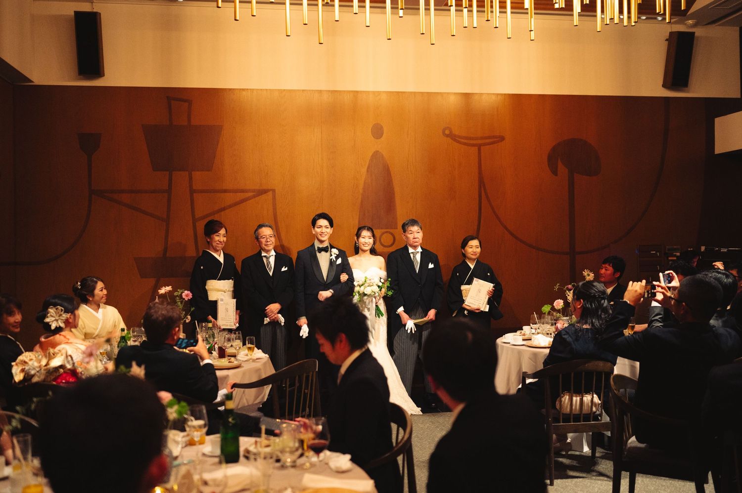 Large banquet hall with hanging lights and guests seated at multiple round tables.