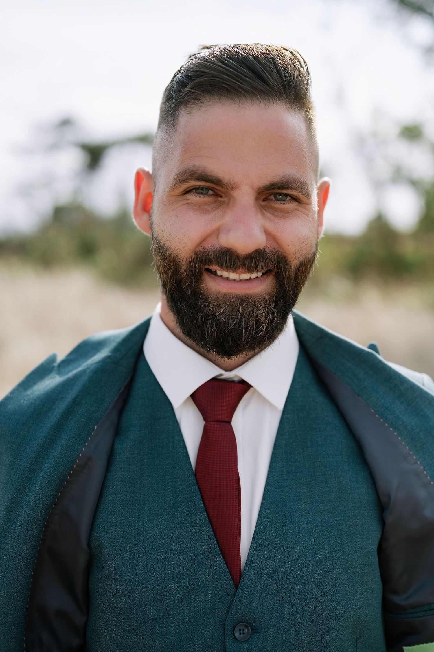 A person in a navy suit and red tie smiles warmly at the camera.