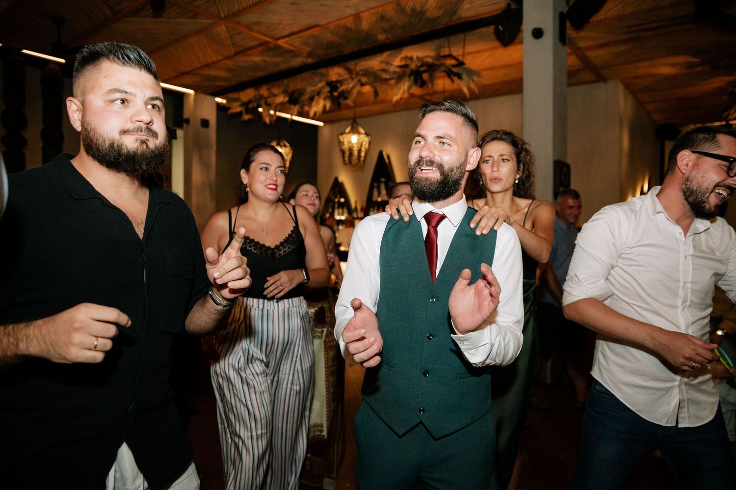 Party guests dancing and socializing in a rustic venue with wooden beams and warm lighting.