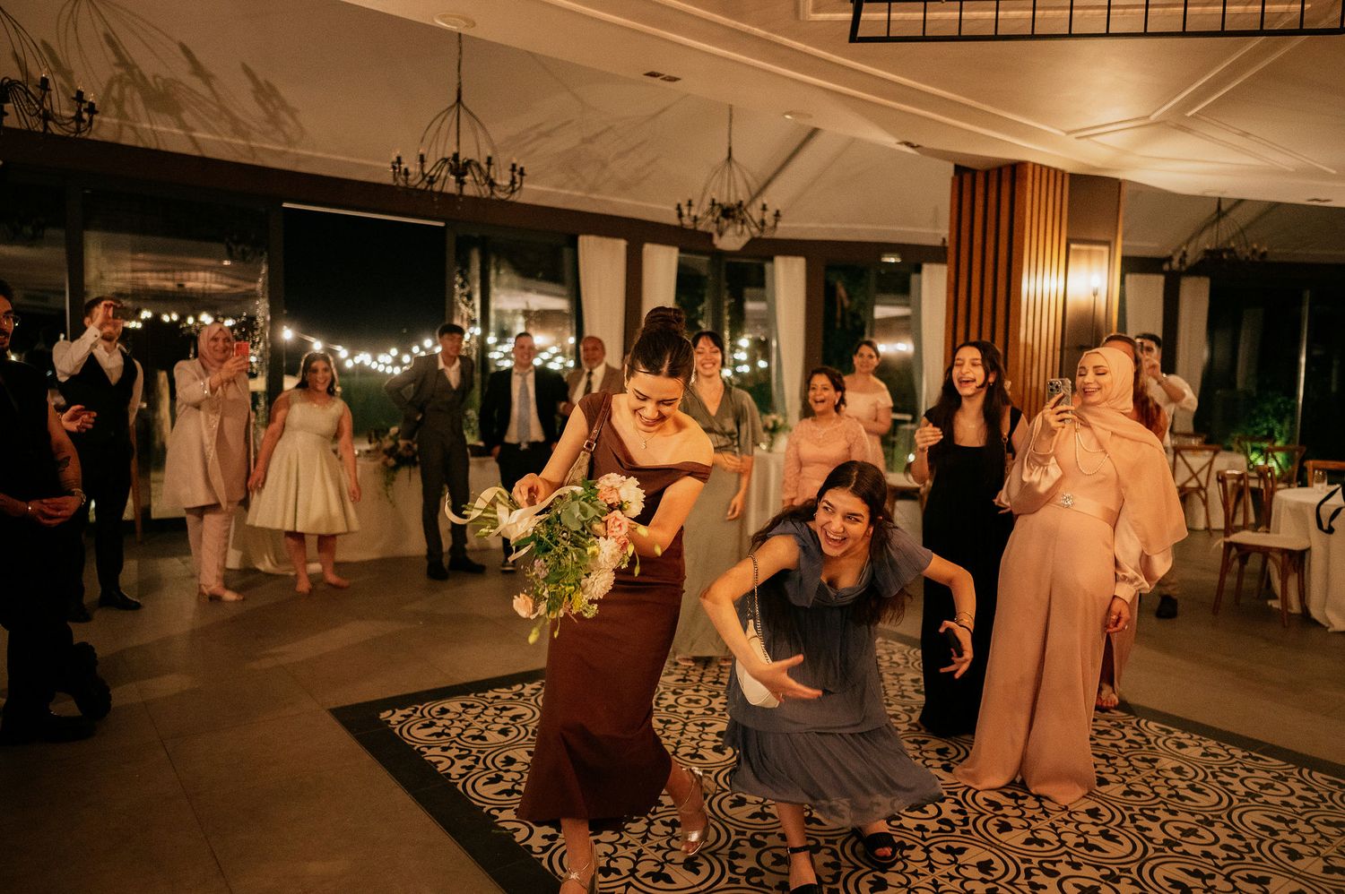 Wedding guests dance and celebrate on a patterned dance floor in an elegant venue.