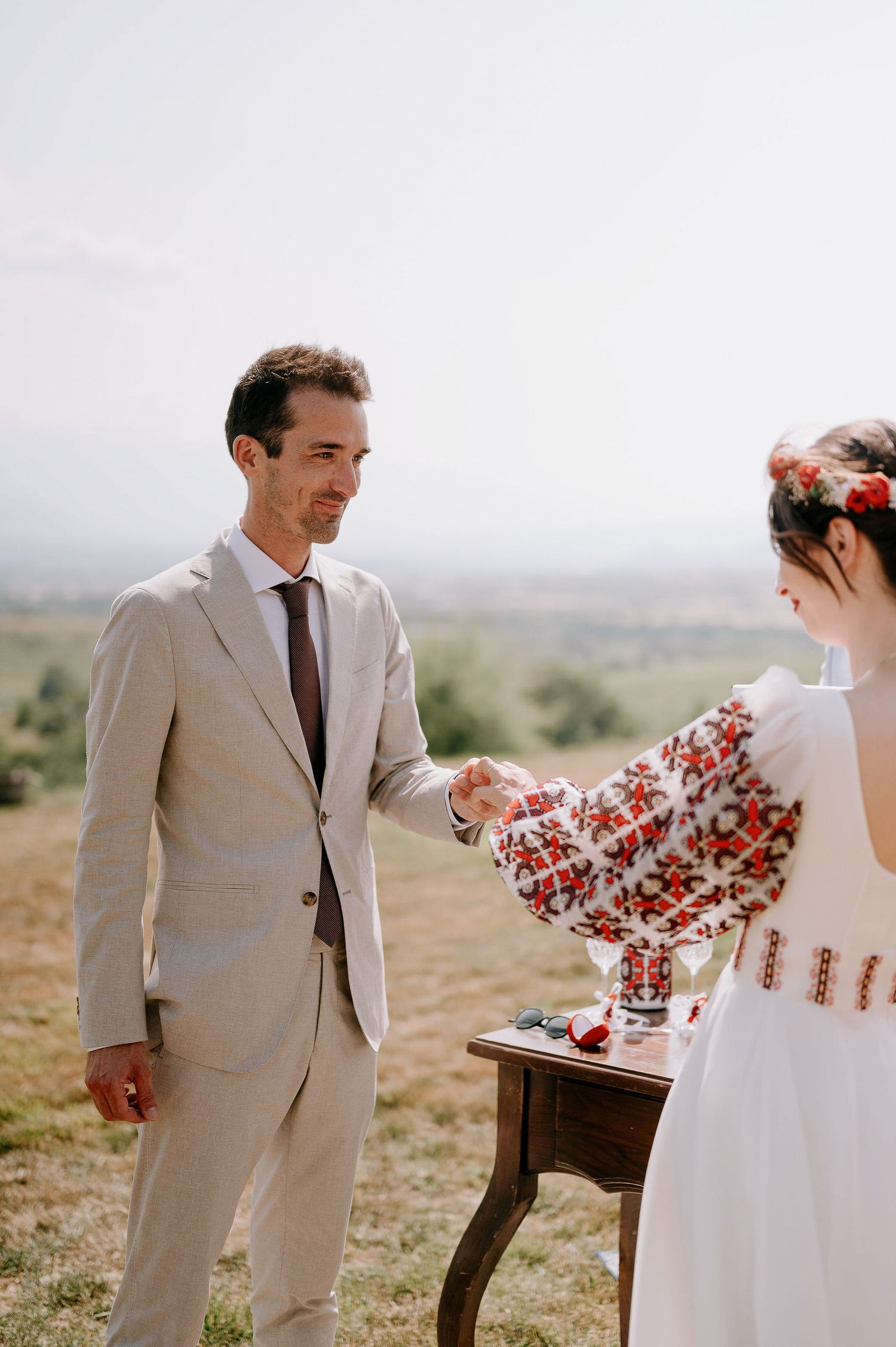 A wedding couple performs a ceremony ritual outdoors with red florals on a rustic table.
