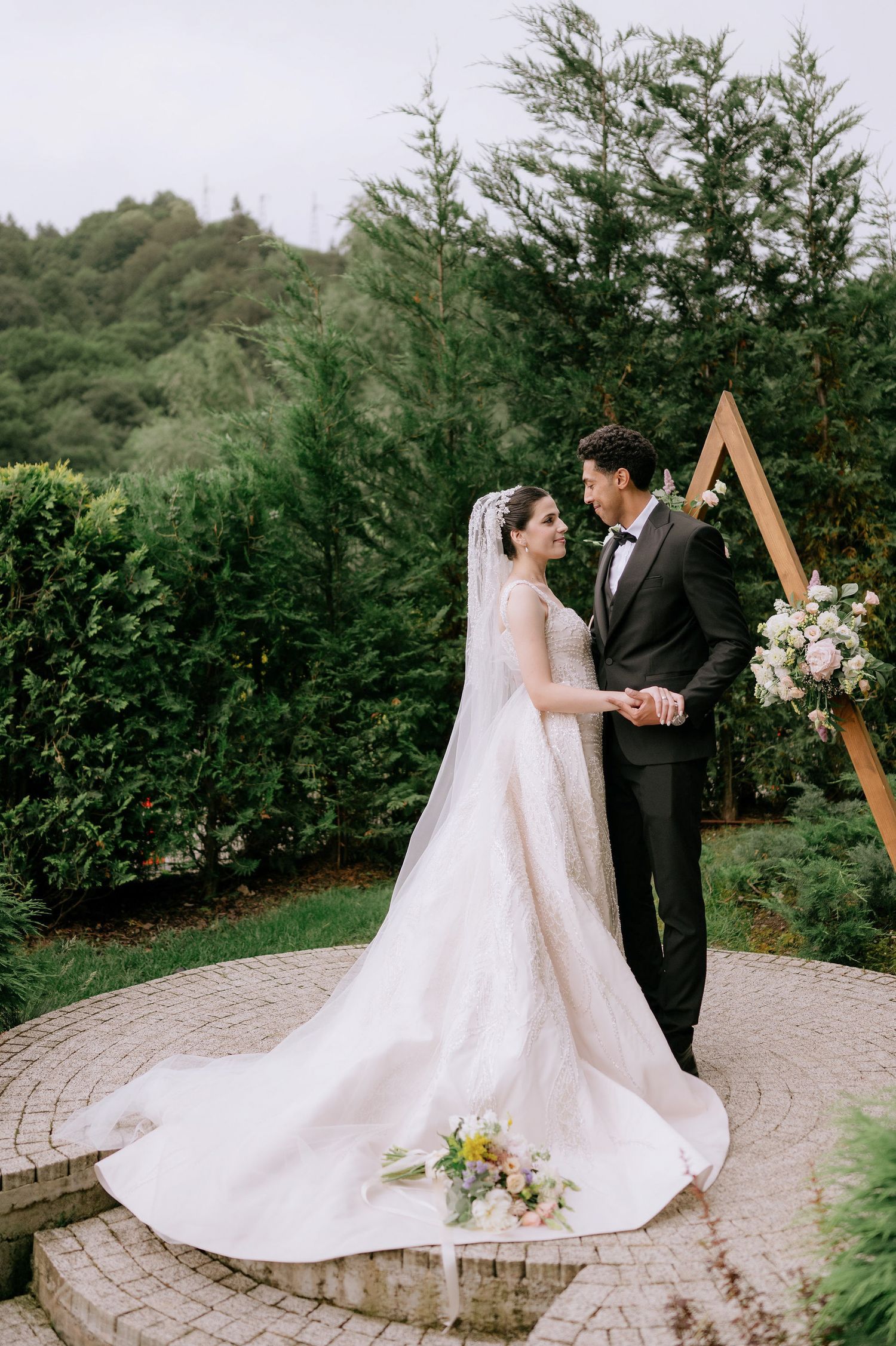 Romantic outdoor wedding scene with geometric arch and lush evergreen backdrop.