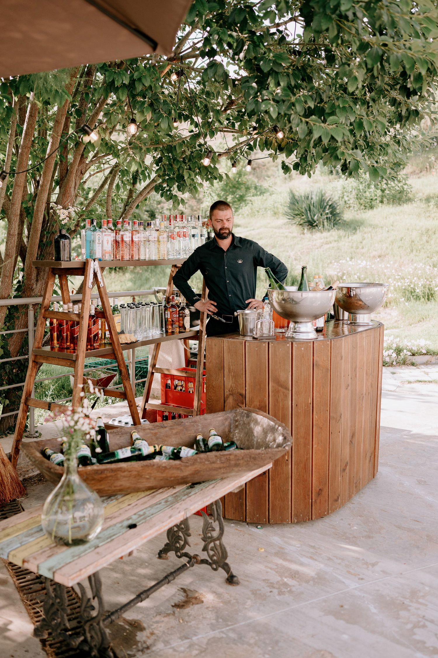 Rustic wooden outdoor bar setup under trees at wedding reception.
