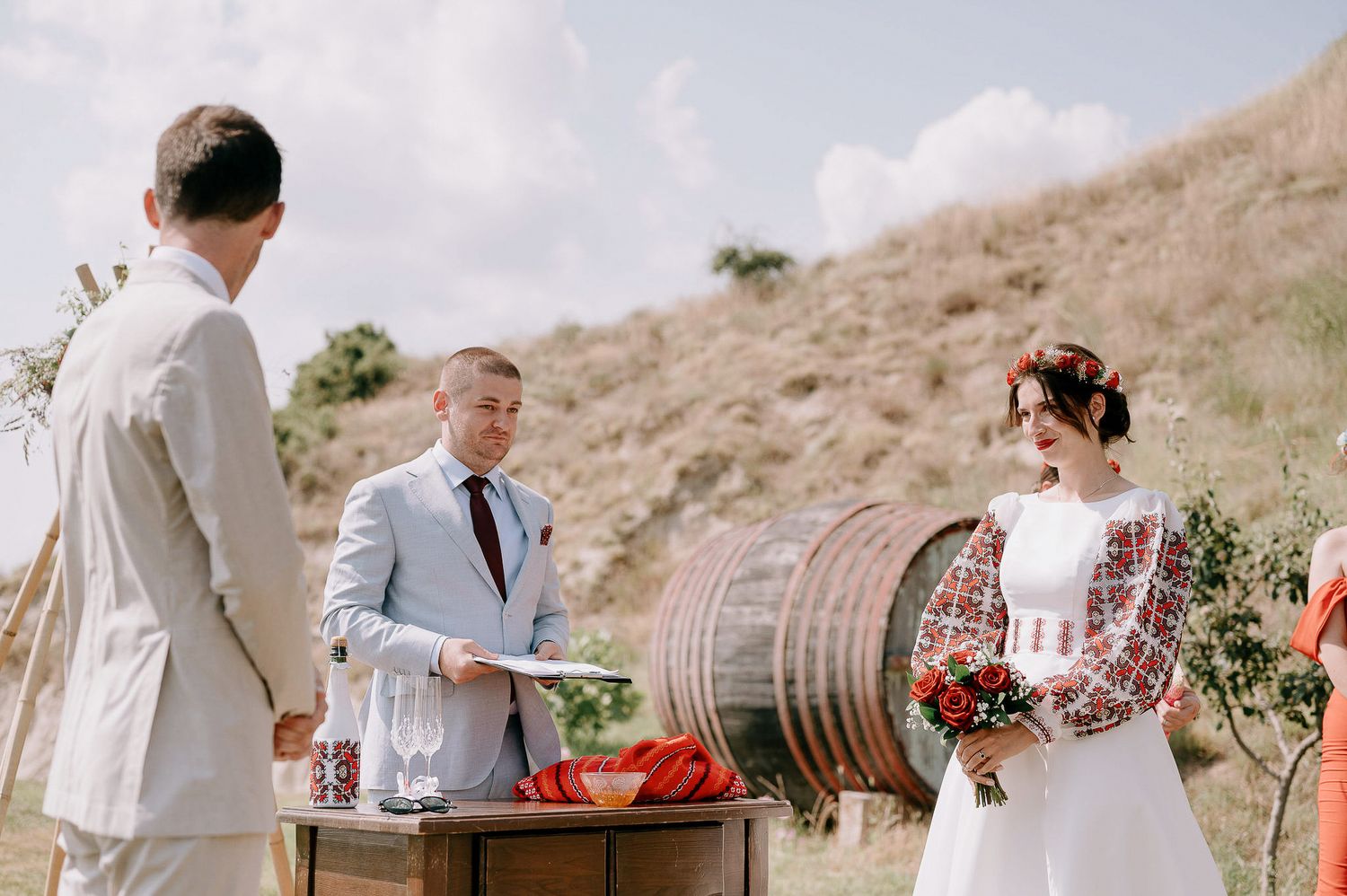 Wedding celebration on hillside with rustic wine barrel and floral decorations.