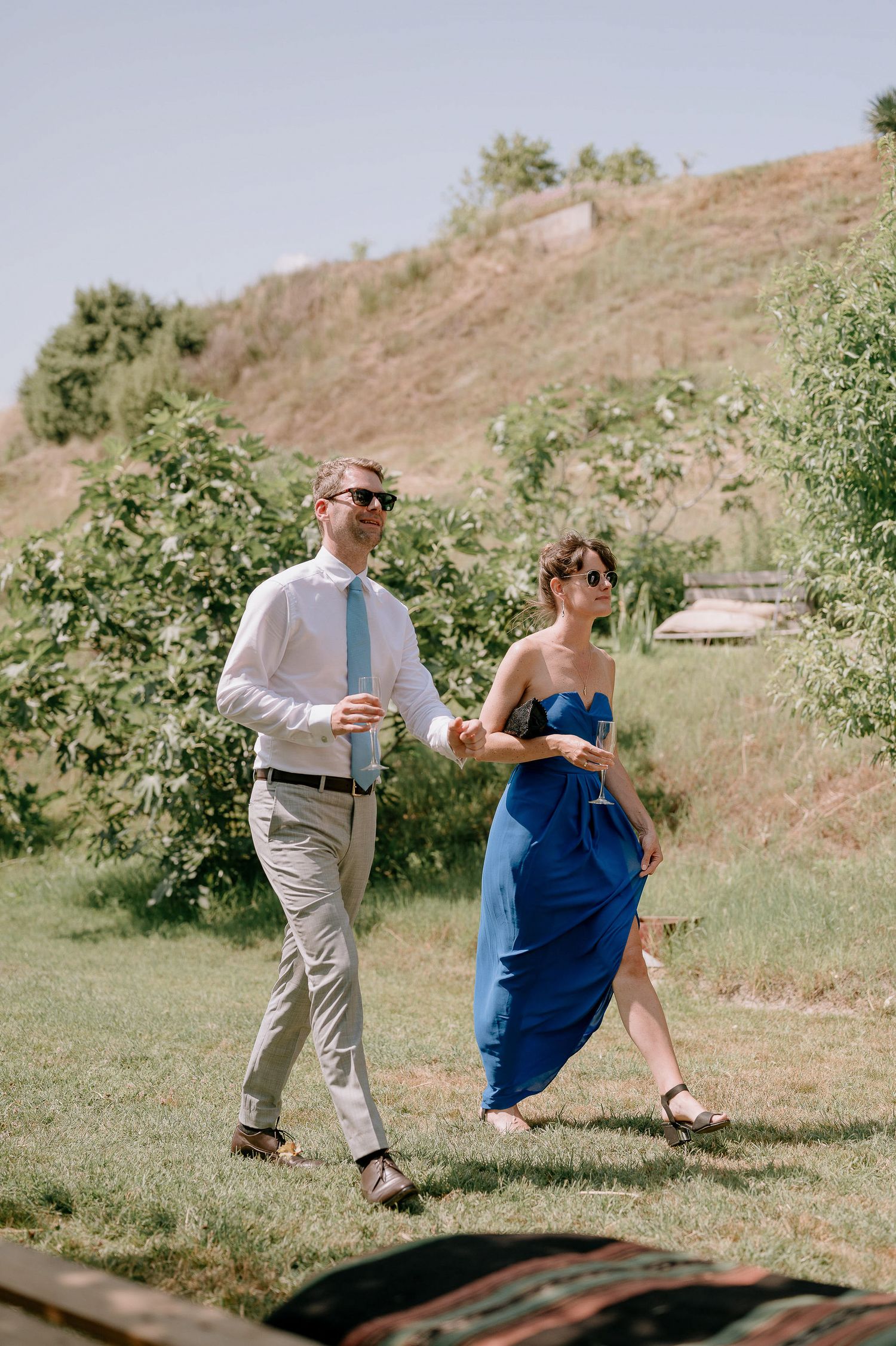 Couple in formal attire dancing on a grassy hillside during a celebration.