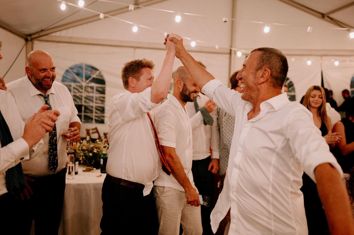 Lively dance party scene with guests celebrating under string lights in a white tent.