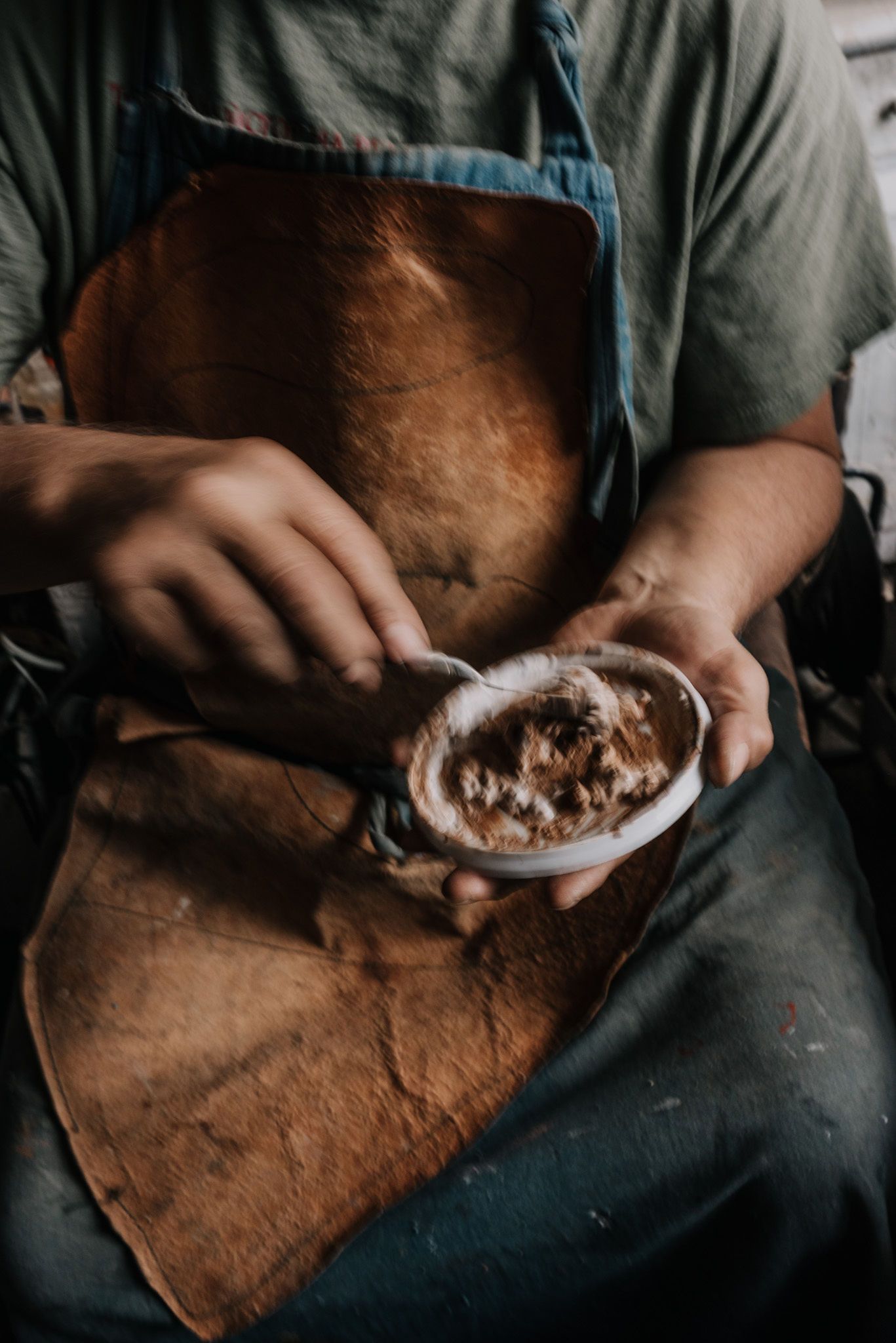 Person in work clothes holds a plate while sitting in an artisan workshop.