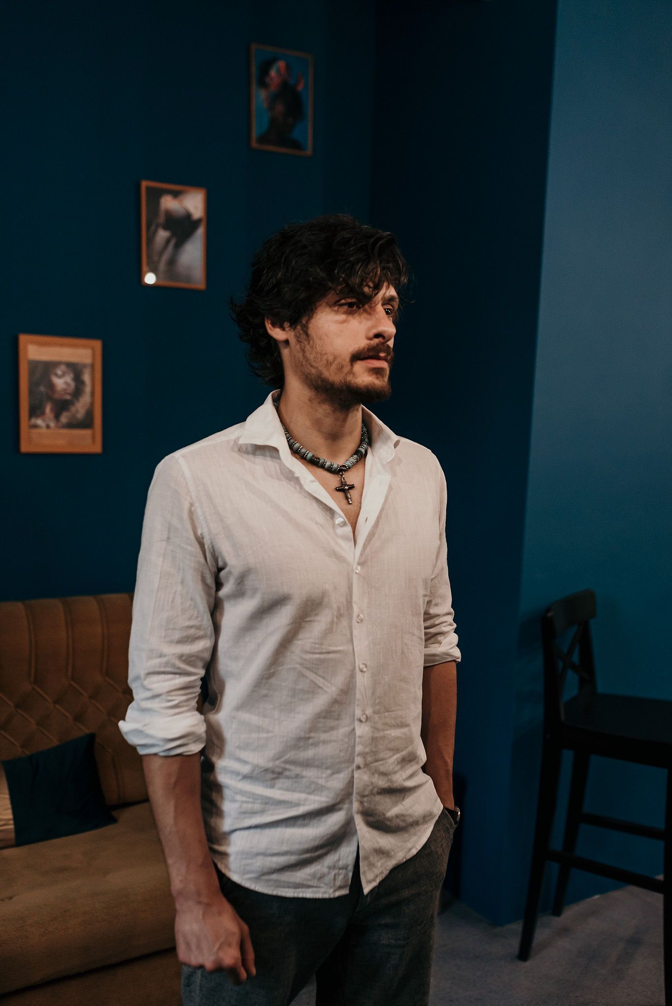 Person in casual white shirt poses against teal wall with vintage photographs.