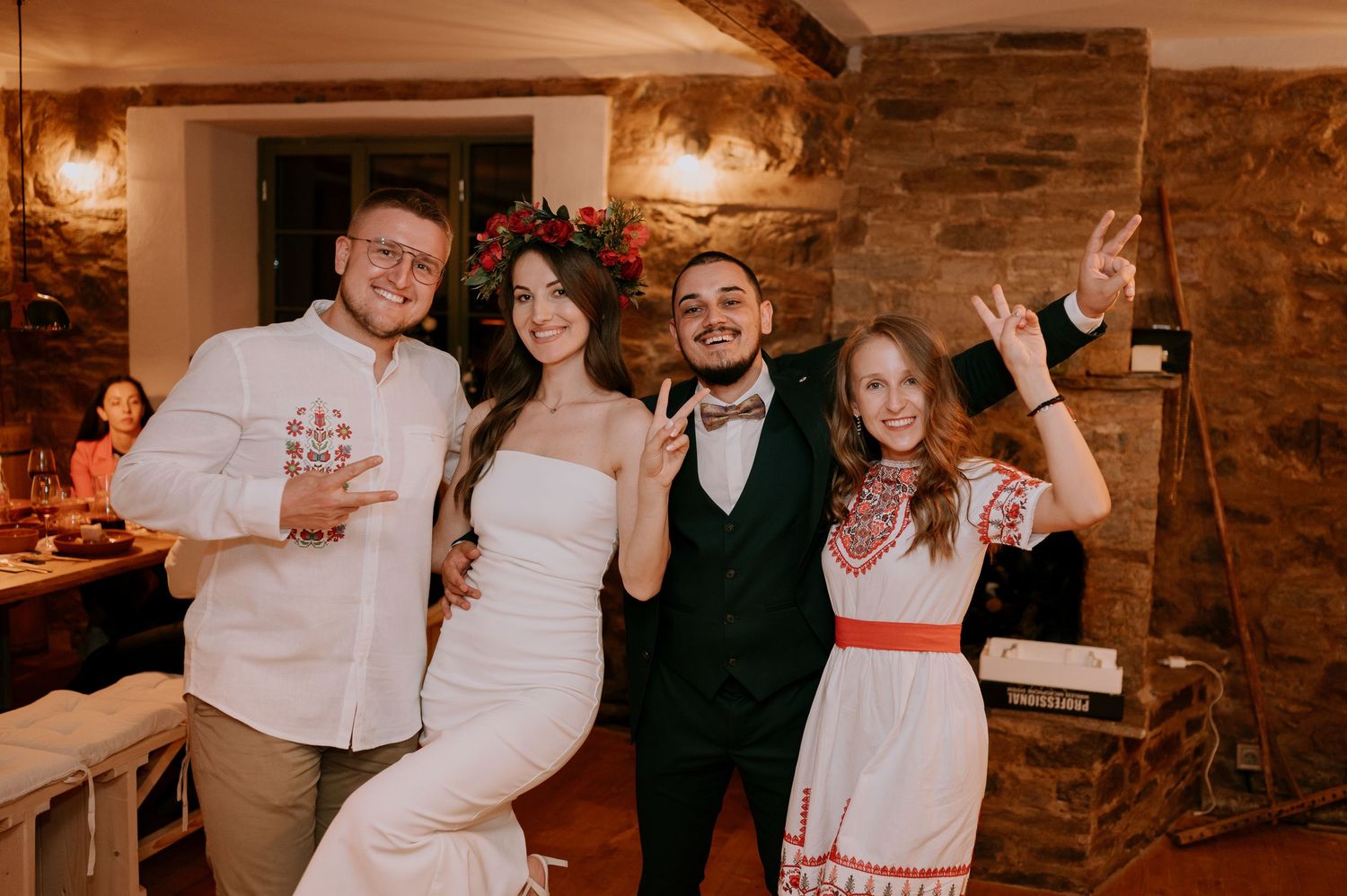 Wedding party members celebrate with drinks and hugs at a rustic indoor venue.
