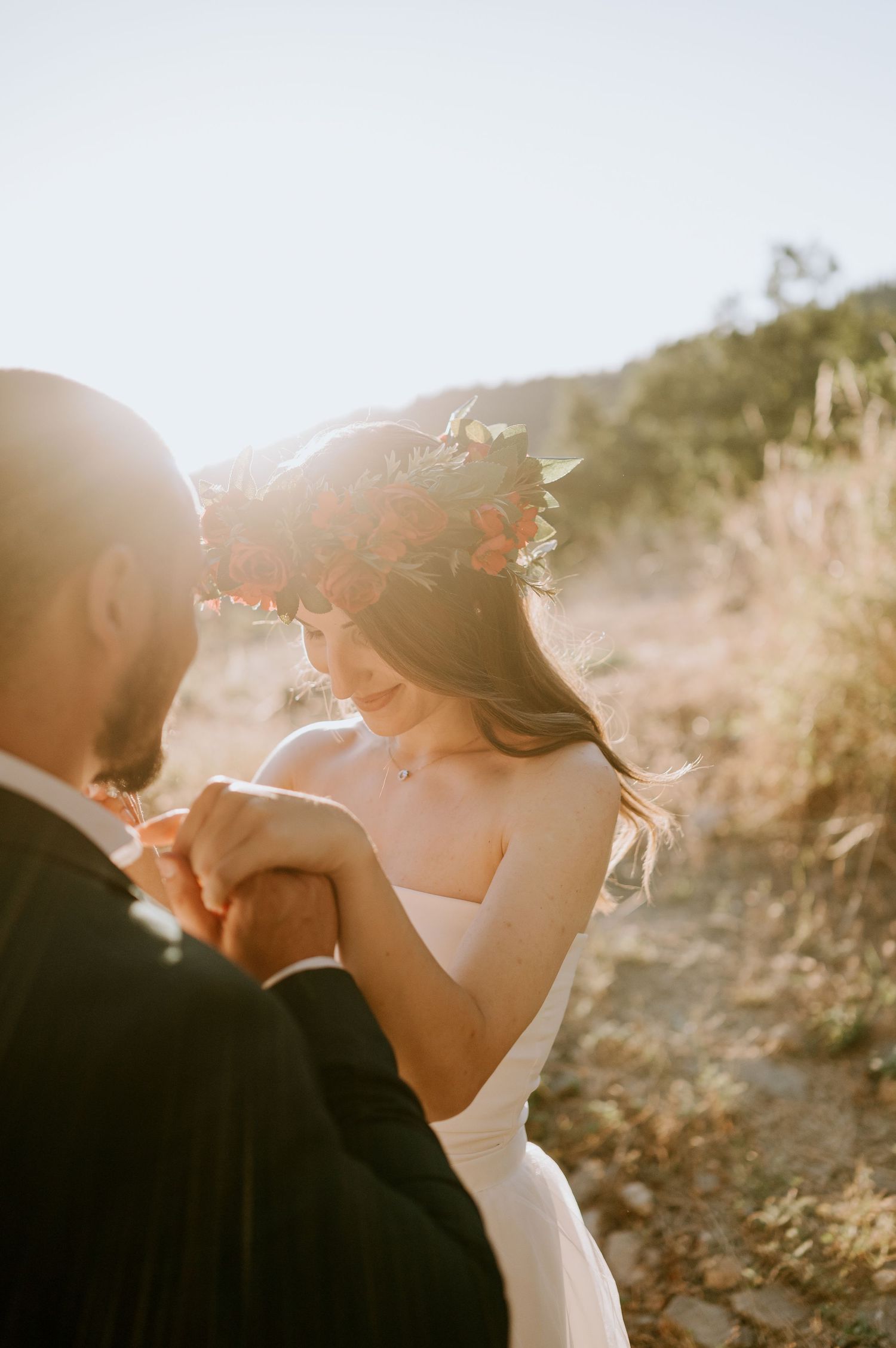Intimate moment between newlyweds during sunset with bride wearing floral crown.