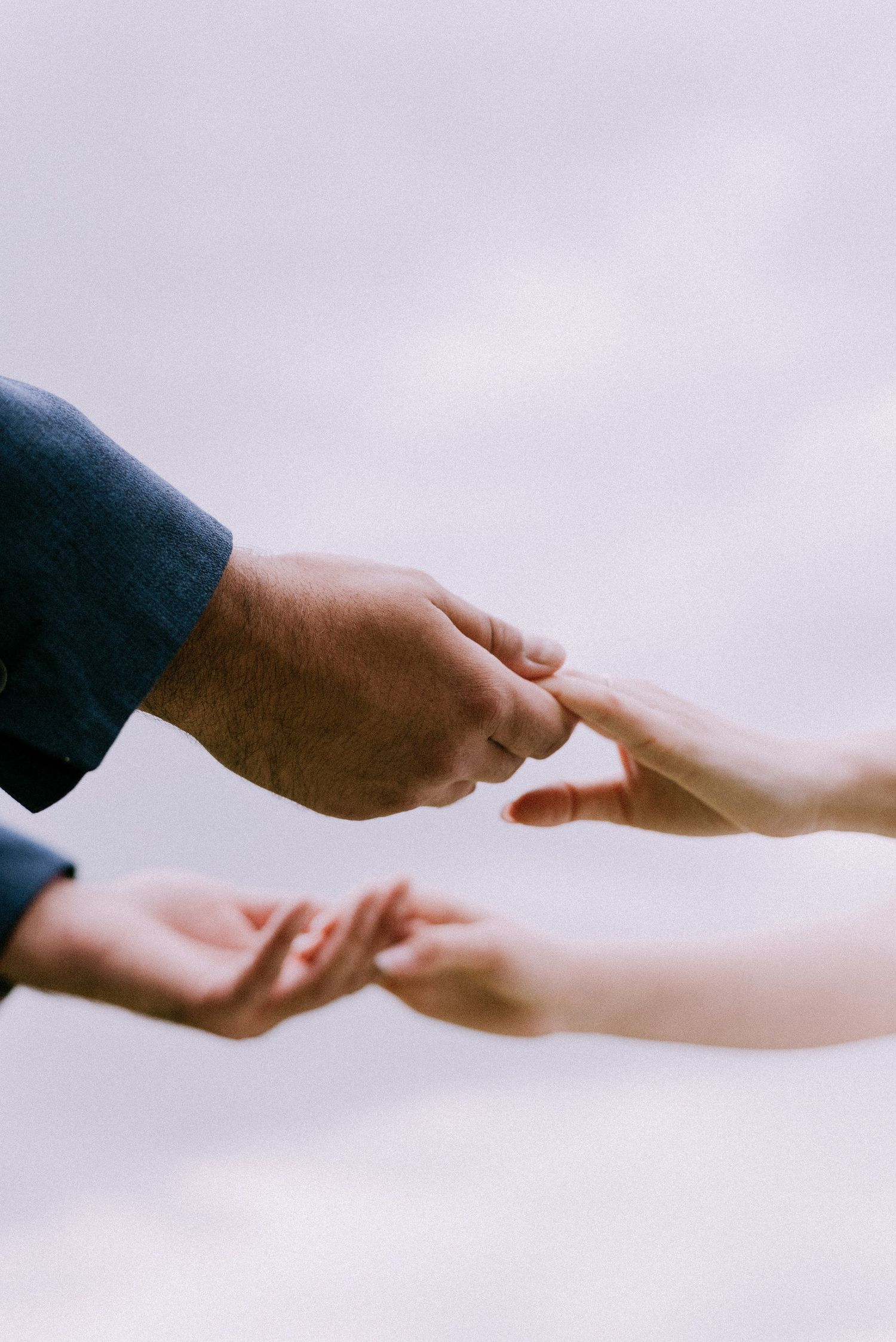 Artistic close-up of hands reaching towards each other against a light background.