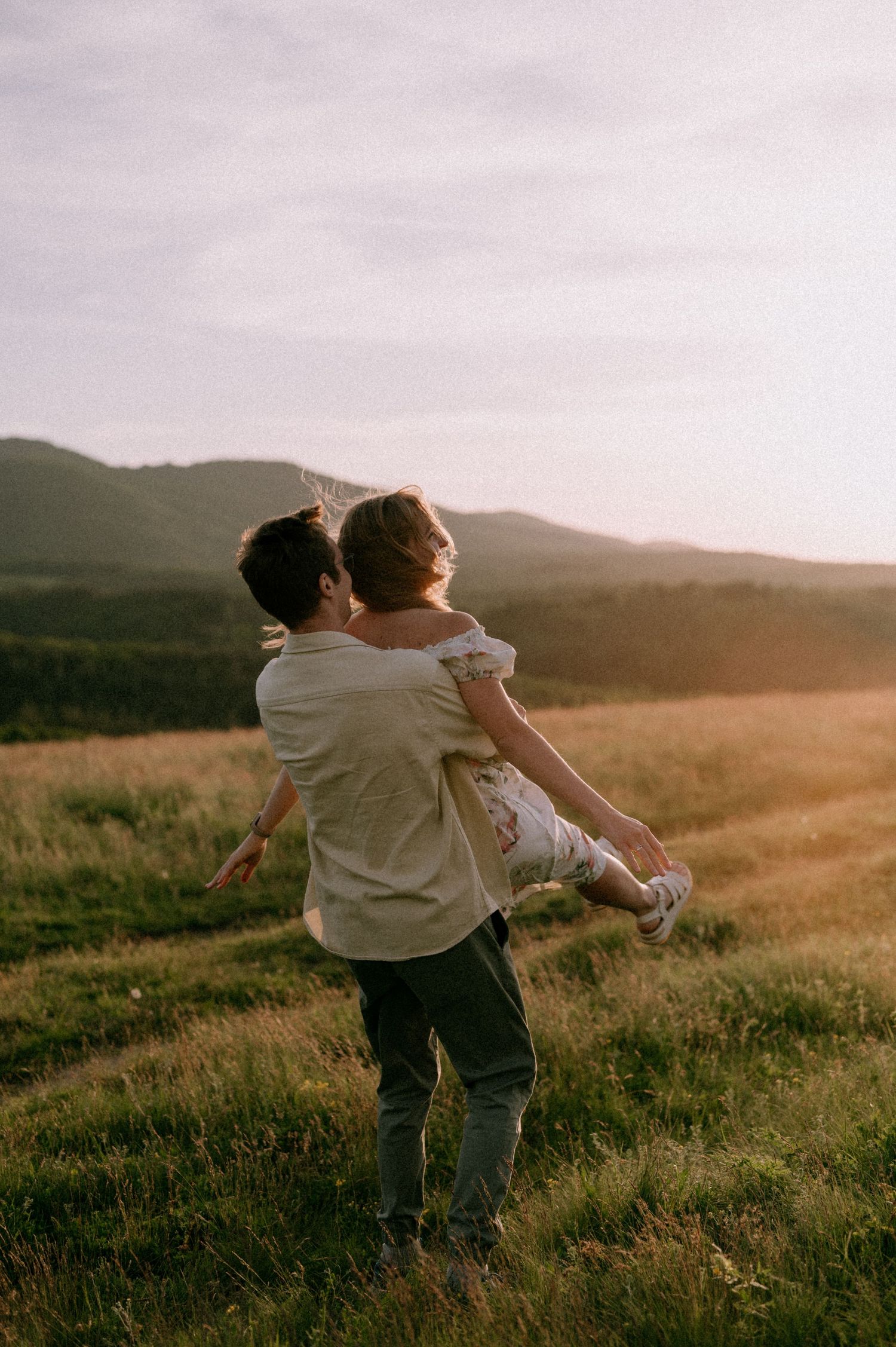 Couple playing and carrying each other in a mountain meadow at sunset.