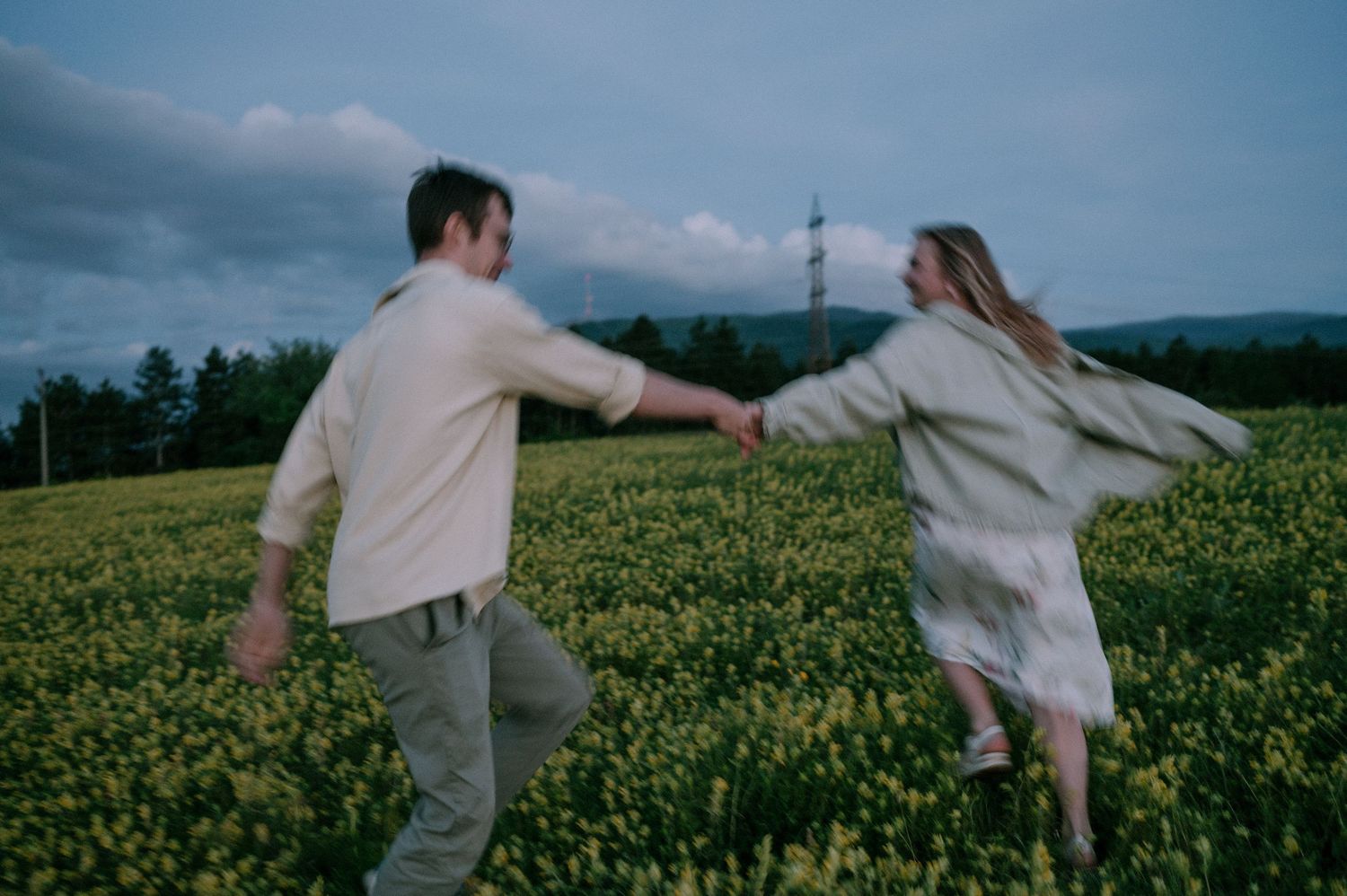 Two people dance carefree through a vibrant yellow canola field.