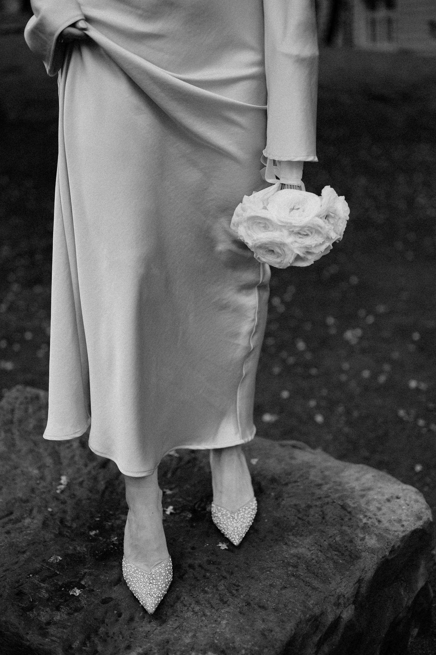 Close-up view of elegant white shoes and dress details on a textured stone surface.