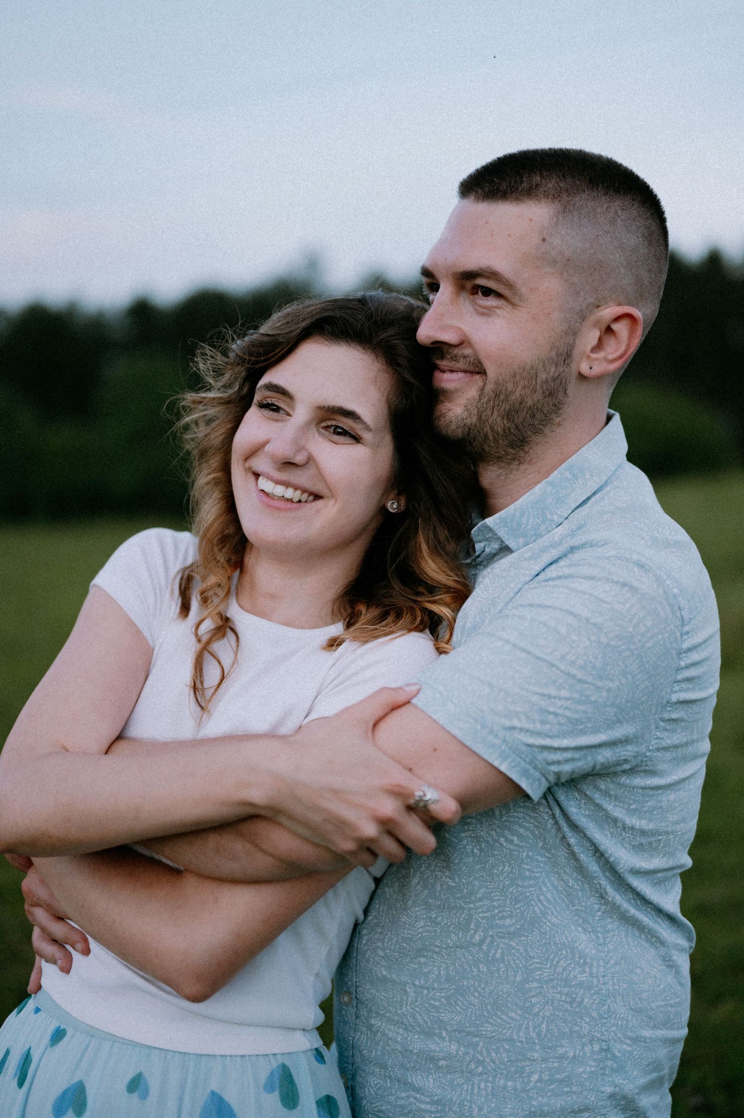 Two people share an intimate embrace while laughing together in a grassy field.