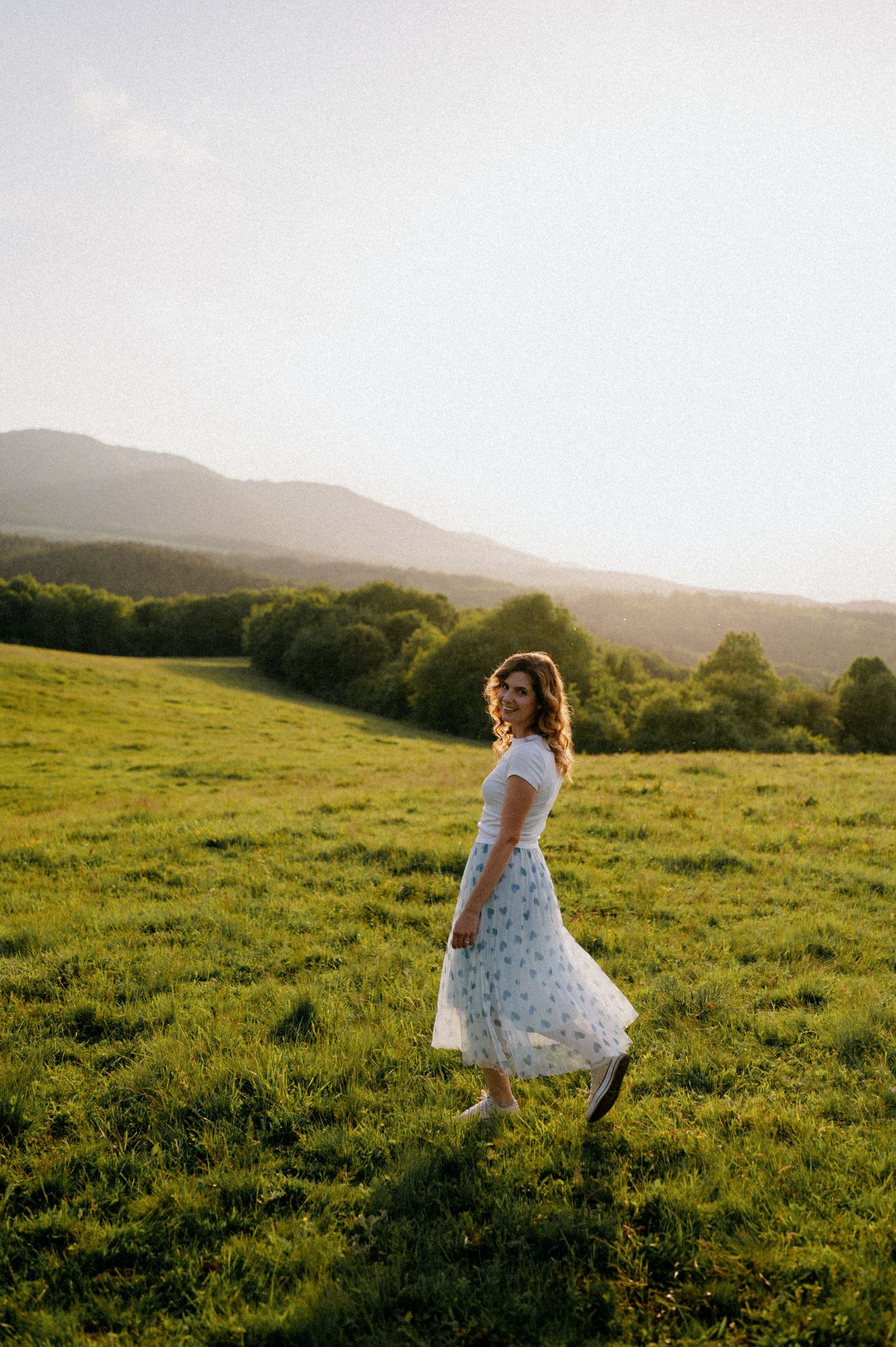A joyful dance in a polka dot dress unfolds on a grassy hilltop at sunset.