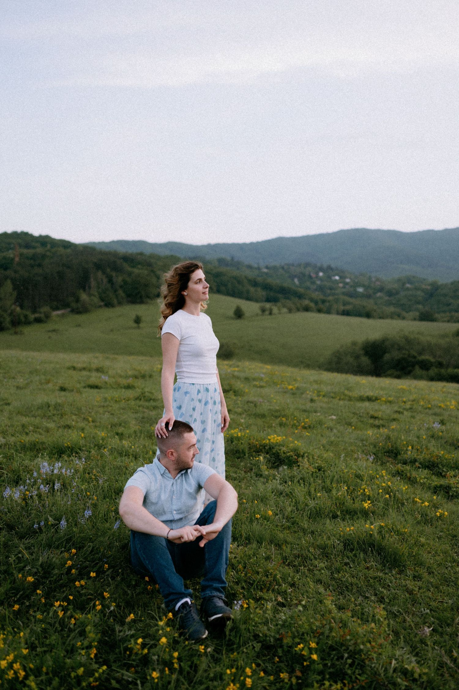 A romantic couple enjoys a peaceful moment in a hilltop meadow with mountain views.