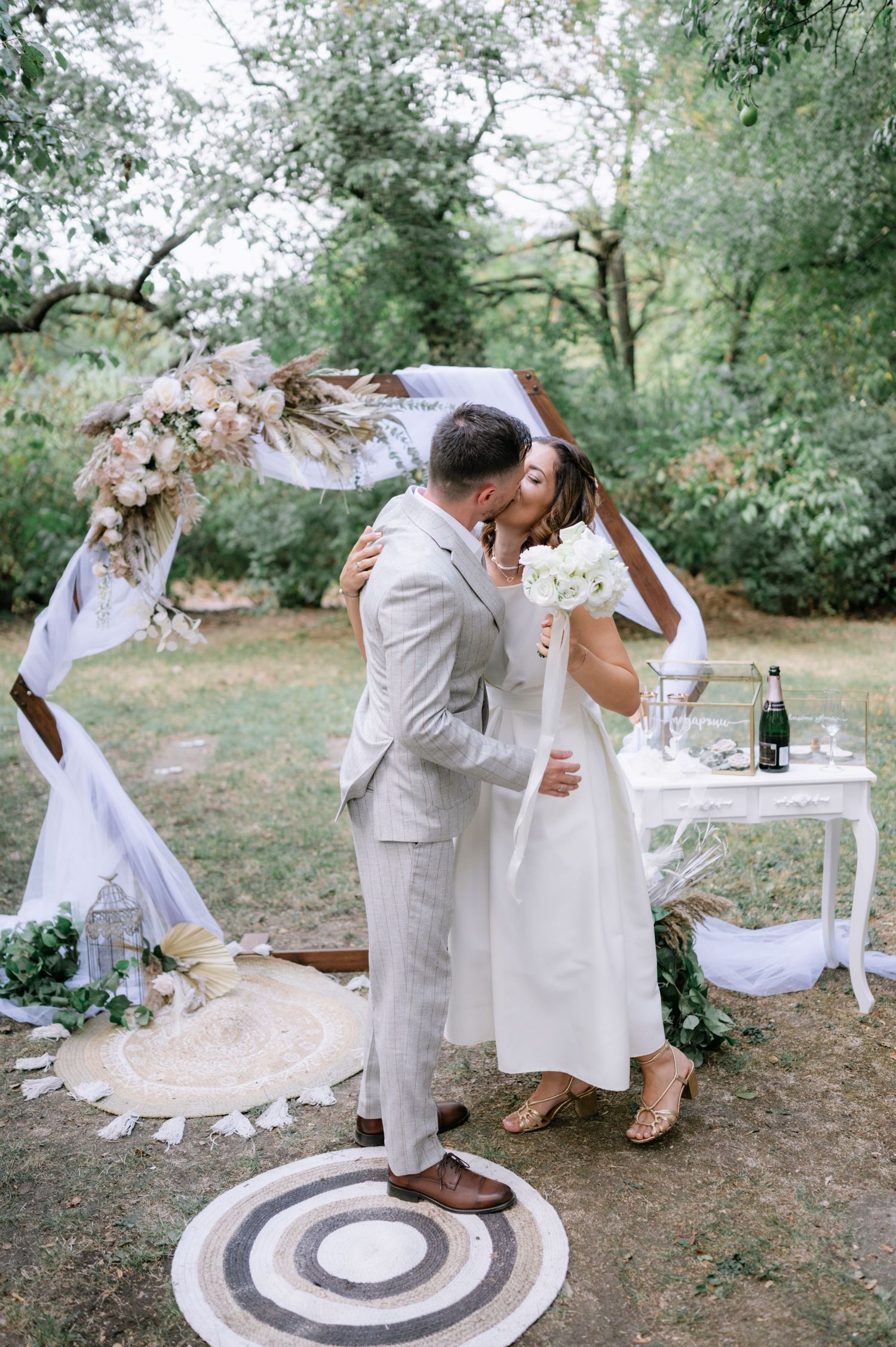 Couple in light colored attire dance together on a circular rug during an intimate outdoor celebration.
