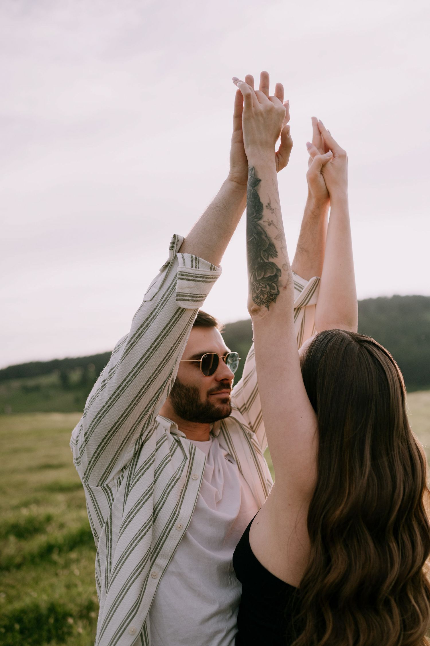 A couple dances together in a field at sunset, with the person in stripes leading a twirl.