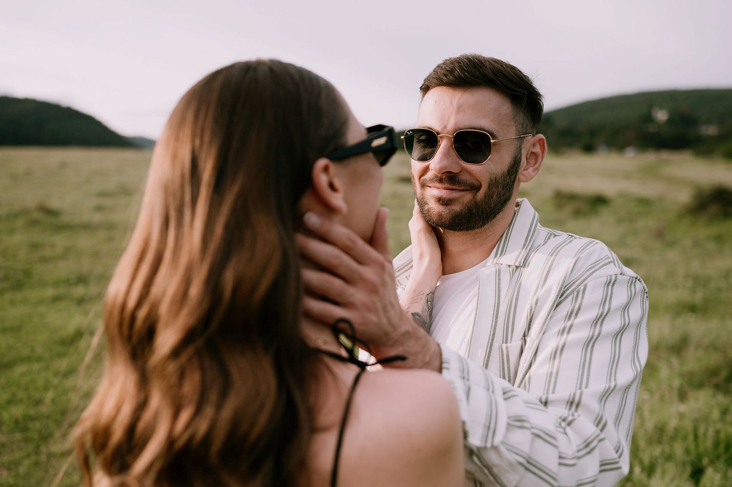 Romantic couple embraces in a sunlit meadow during a golden hour photoshoot.