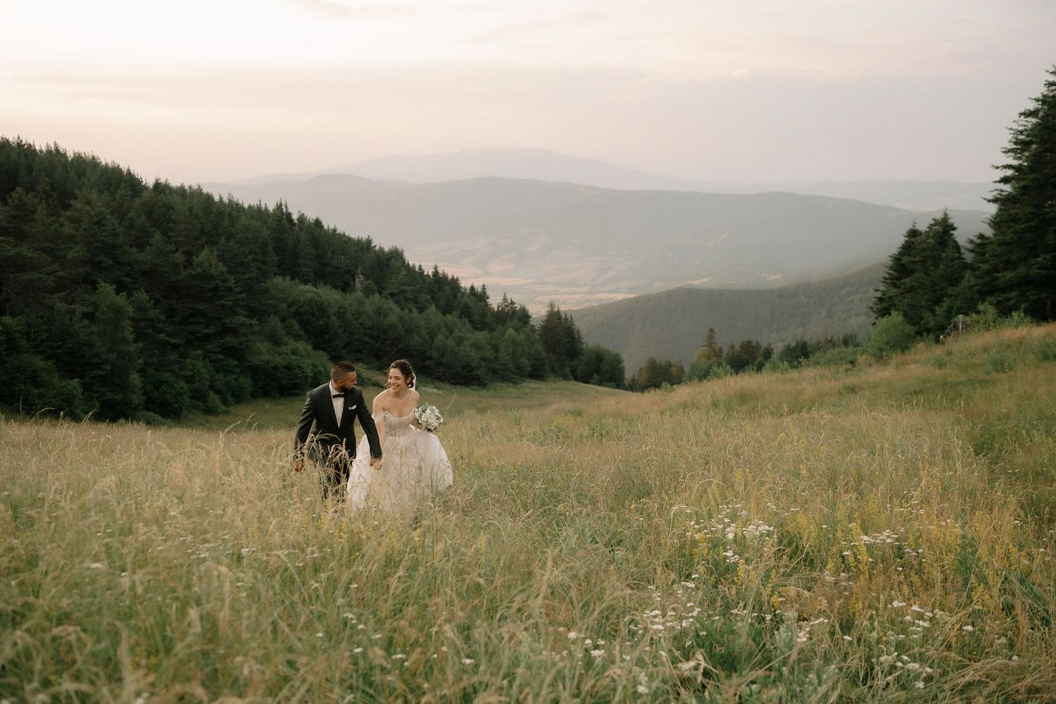 A scenic mountain landscape with rolling hills and meadows captured at golden hour with wildflowers in the foreground.
