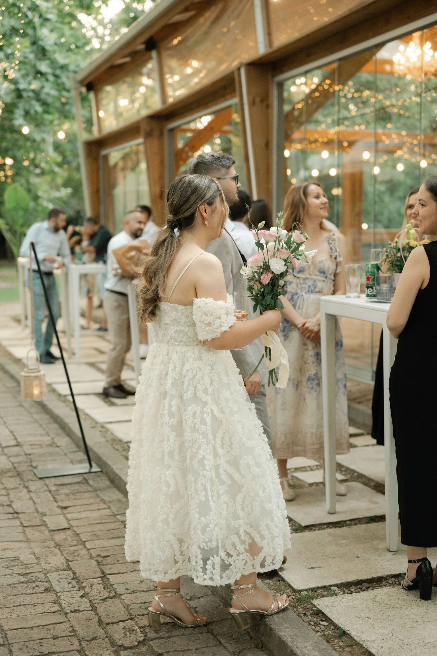 Wedding guests gather on a stone patio with string lights overhead during an elegant outdoor reception celebration.