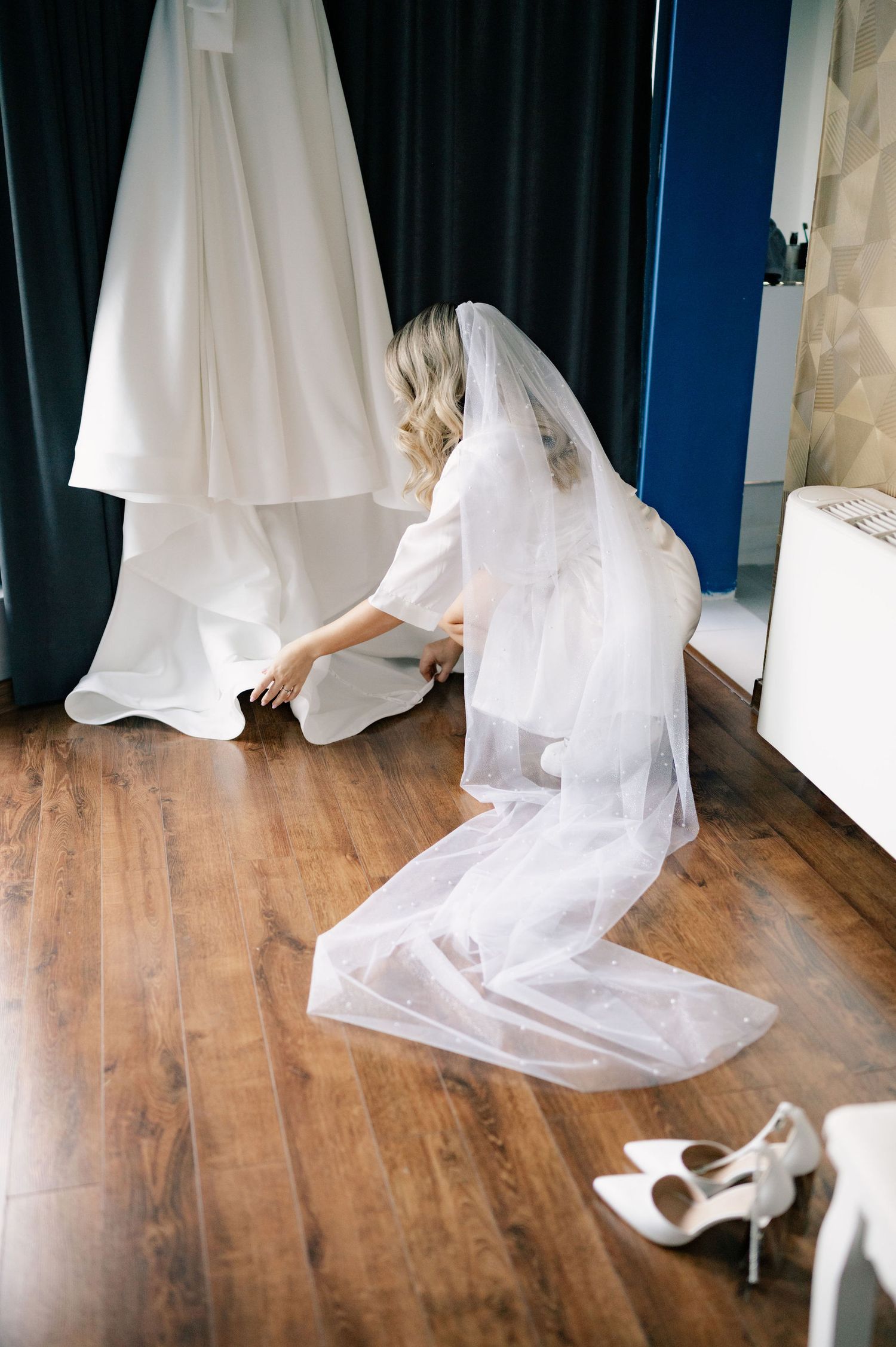 Multiple white wedding dresses hang in a row on hangers against a dark backdrop with wooden flooring visible below.