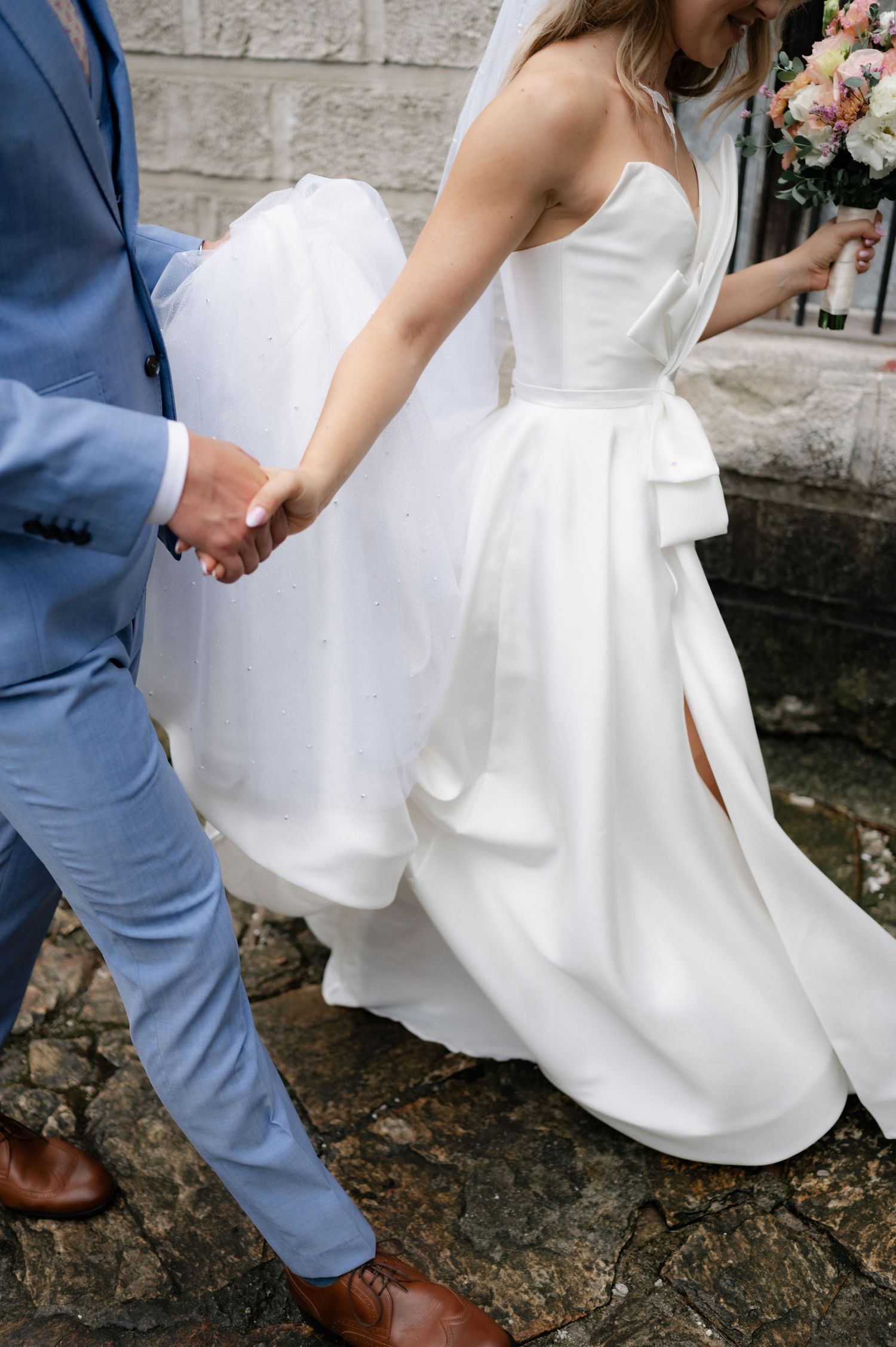 Close-up shots of a couple's feet showing brown leather dress shoes and a flowing white wedding dress on stone ground.