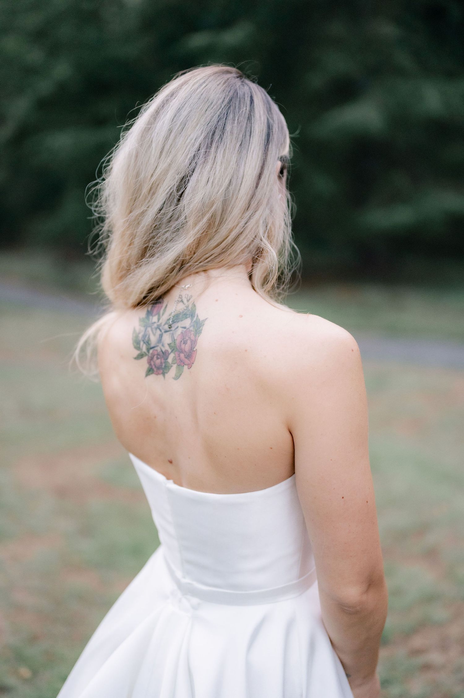A person with blonde hair and a white dress shows off a back tattoo in an outdoor setting.