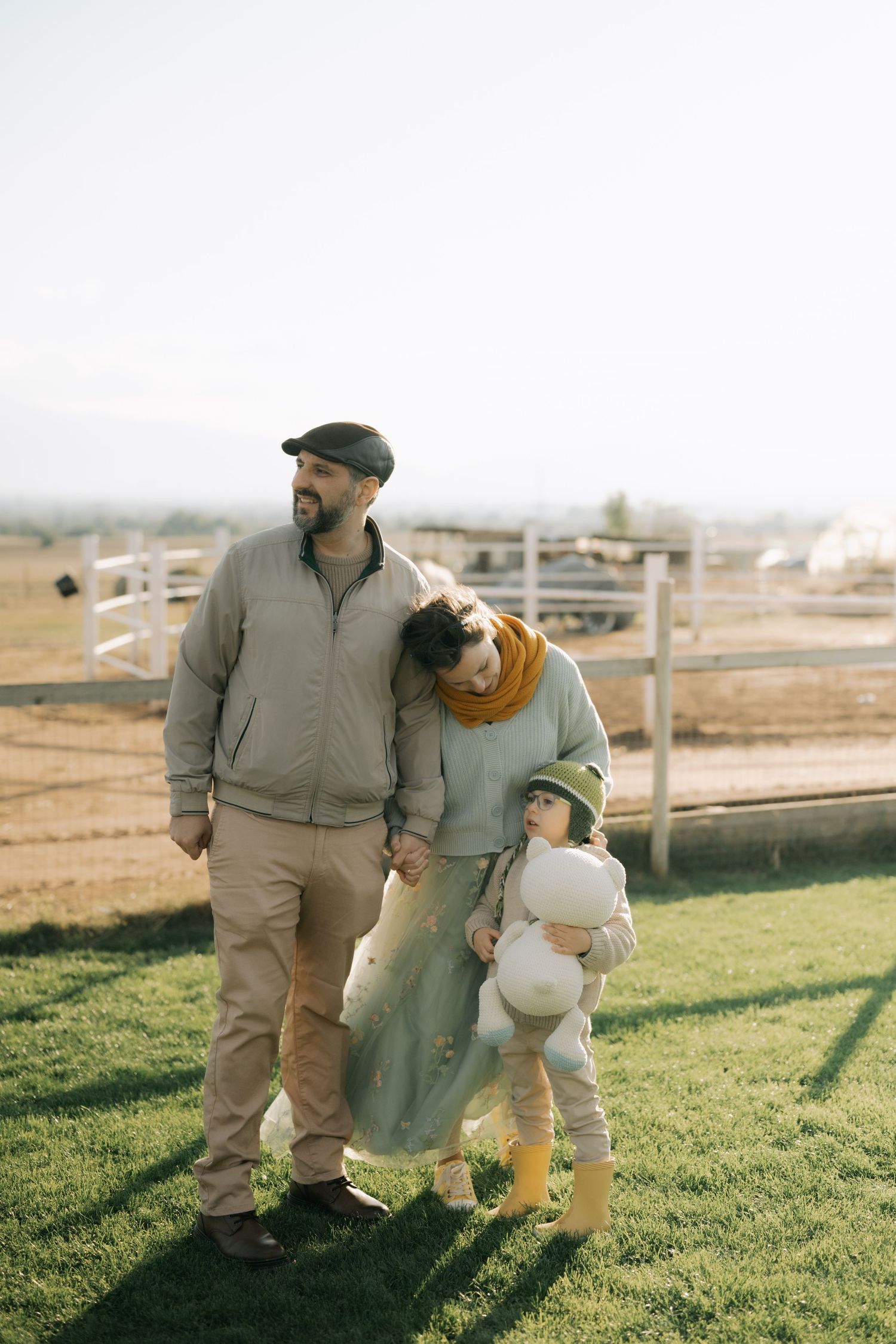 A couple and their dog walk together across a grassy field on a sunny afternoon.
