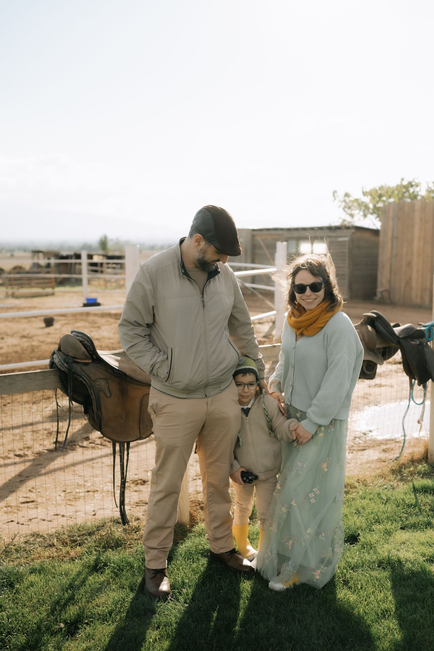Two people interact with horses at a sunny ranch, capturing a casual moment in an outdoor equestrian setting.