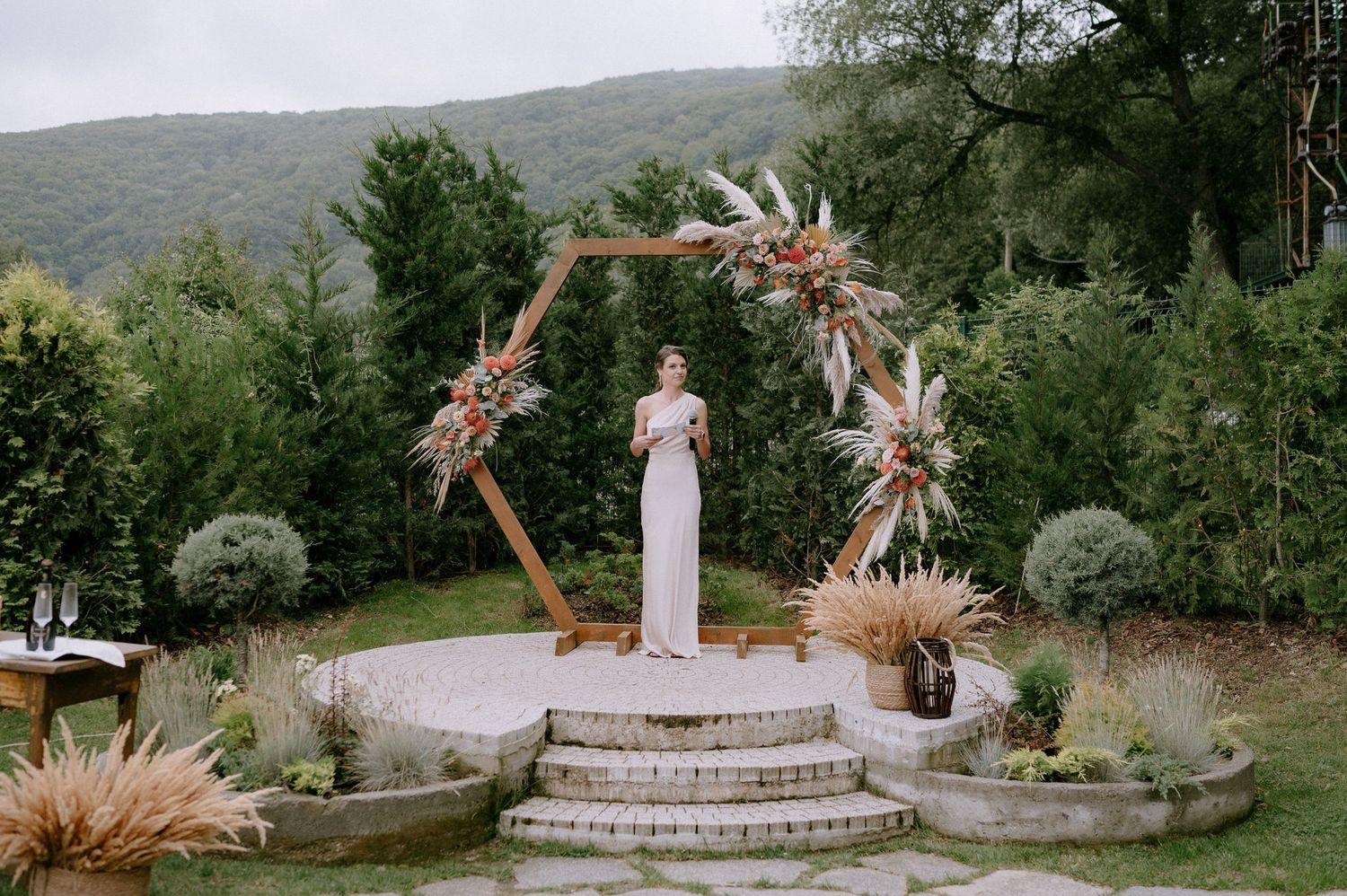 Outdoor wedding ceremony setup with dried palm fronds and white seating arrangements in a natural mountain setting.