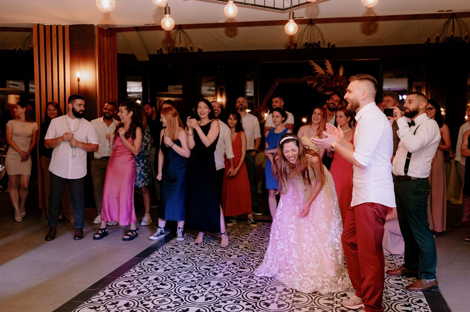 Guests dancing on a patterned black and white dance floor at a formal event with warm lighting and decorative elements.