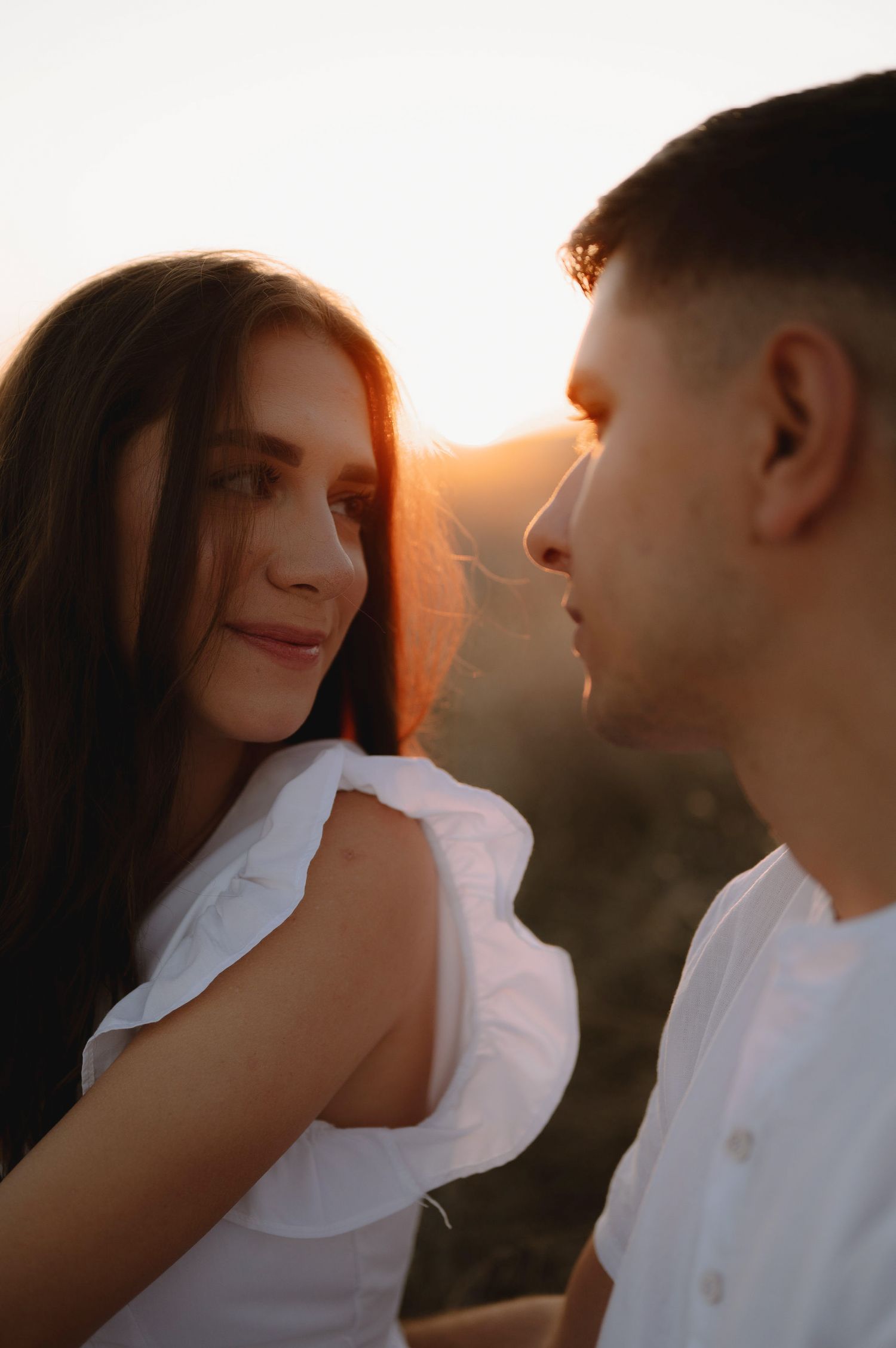 A romantic couple shares an intimate moment at sunset with warm golden light illuminating their silhouettes.