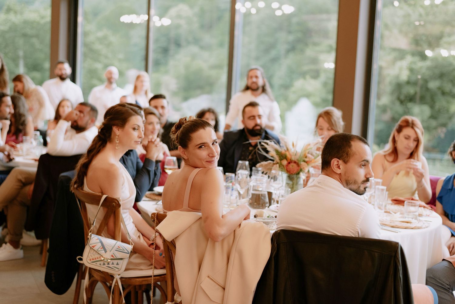 Wedding guests seated at tables during an elegant indoor reception with soft natural lighting and festive atmosphere.