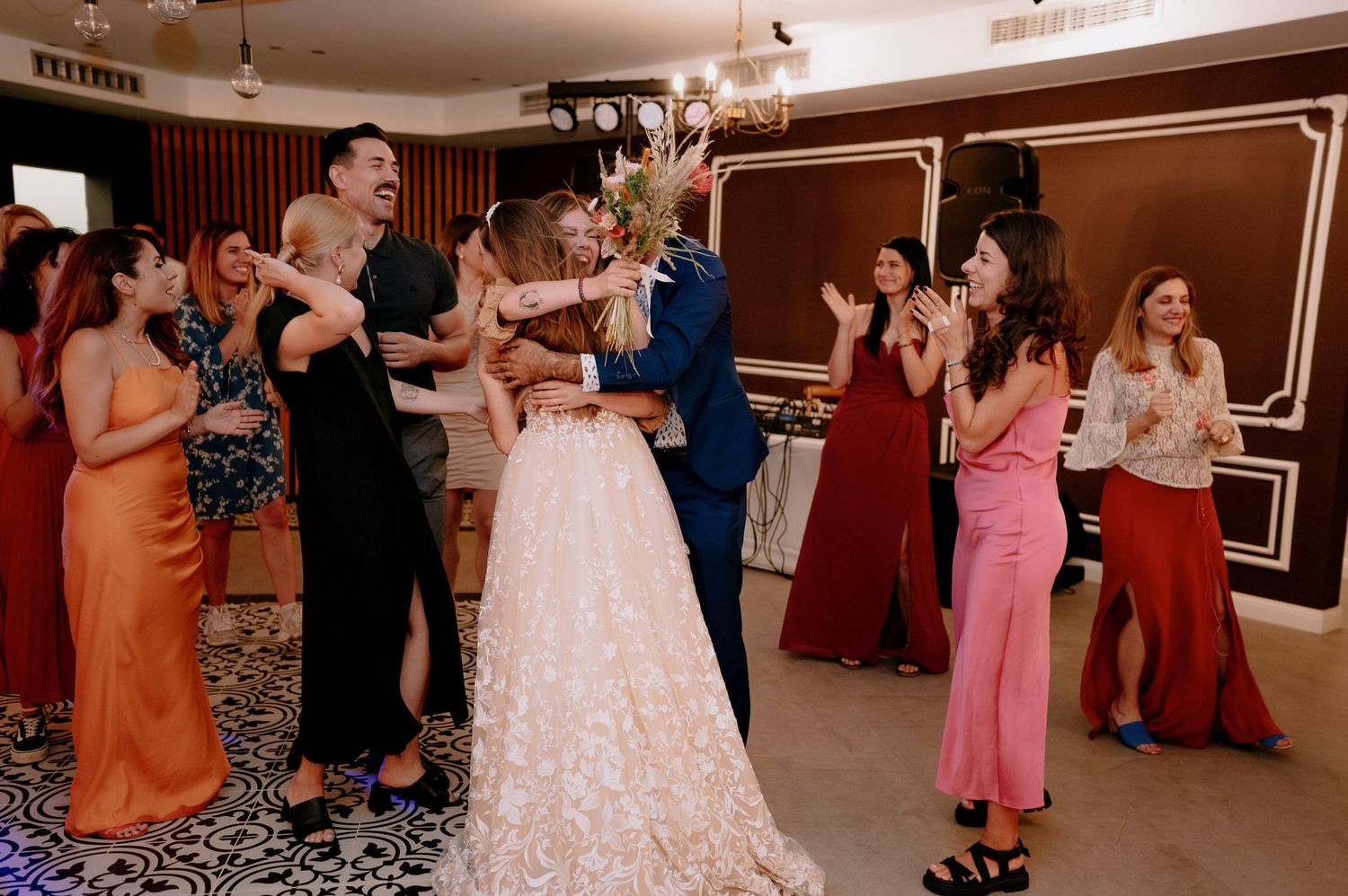 Guests dance and celebrate at an indoor wedding reception with wood paneled walls and warm lighting.