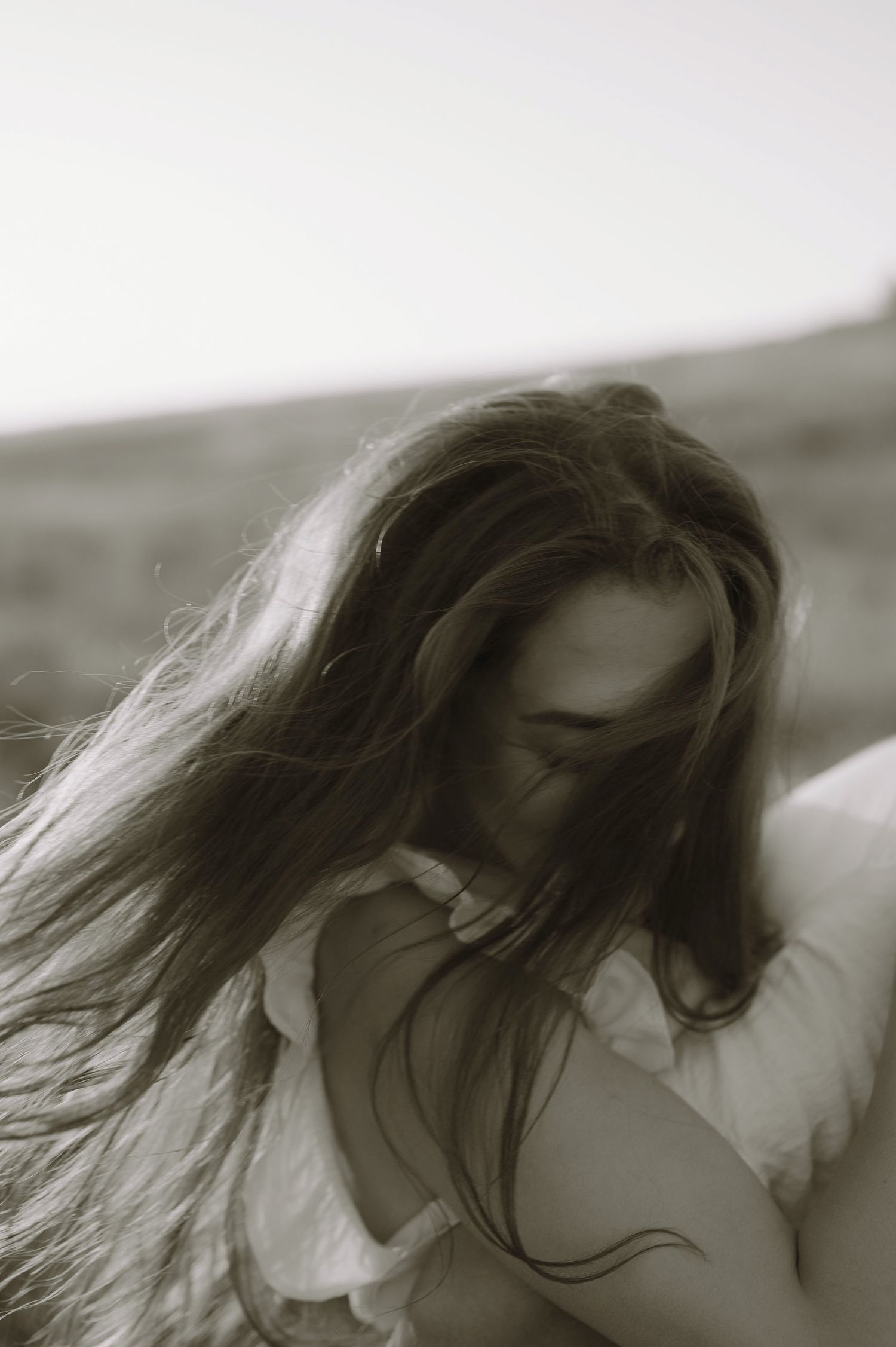 Black and white artistic portrait of flowing dark hair and white fabric in soft natural lighting.