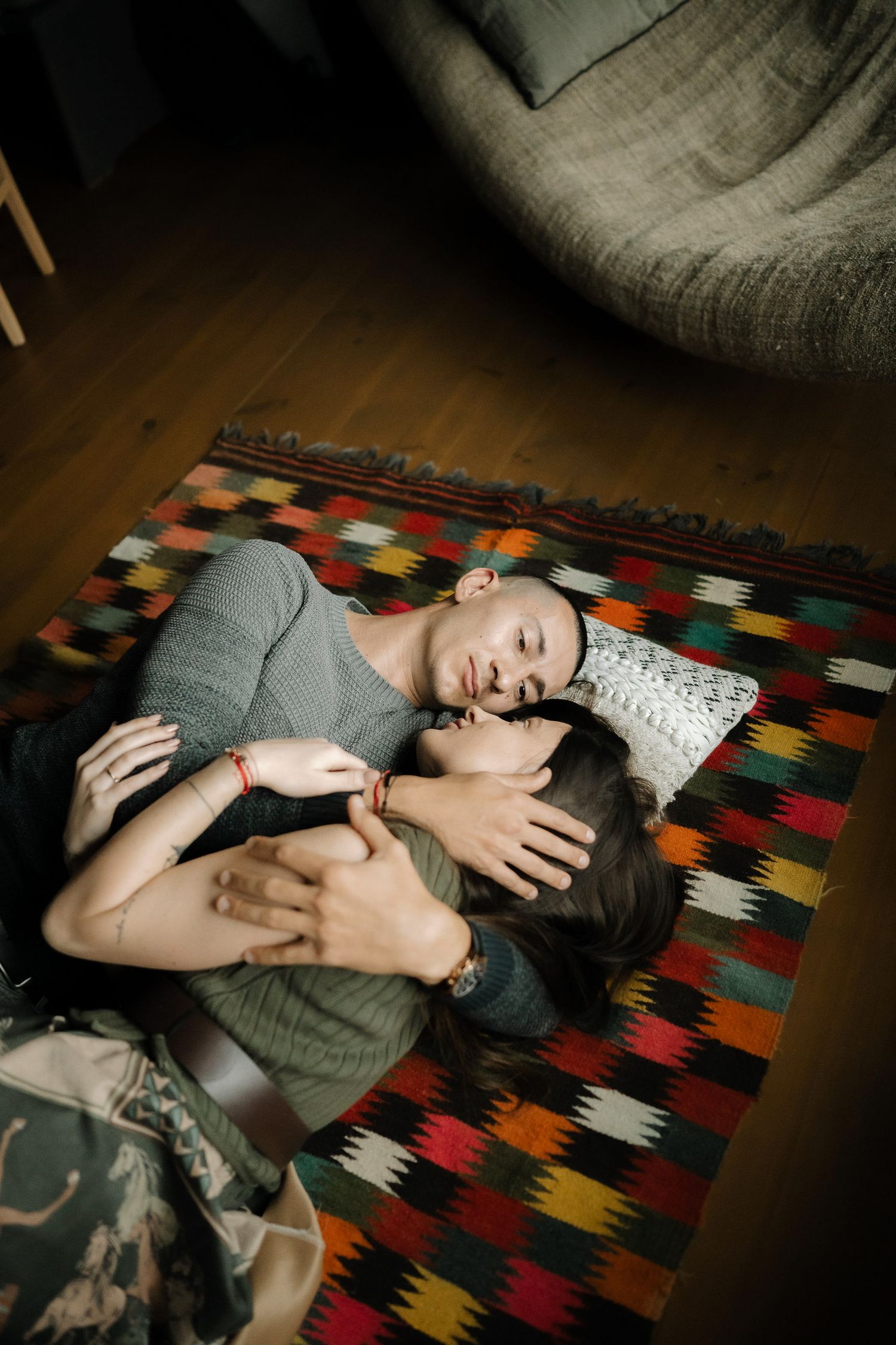 Two people lying close together on a colorful patterned rug in an intimate embrace on hardwood floor.