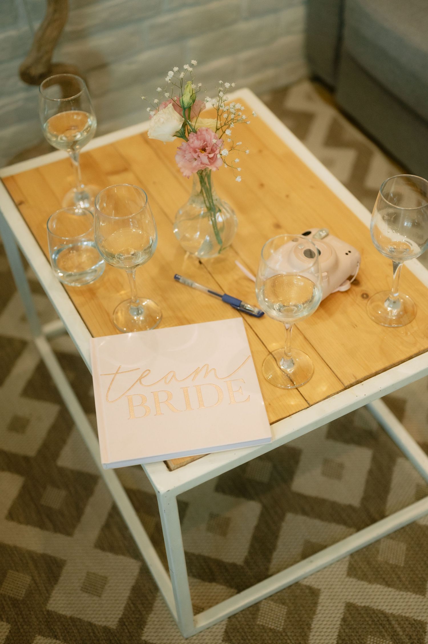Elegant wedding place setting details with delicate pink flowers in small vases on white and natural wood tables.