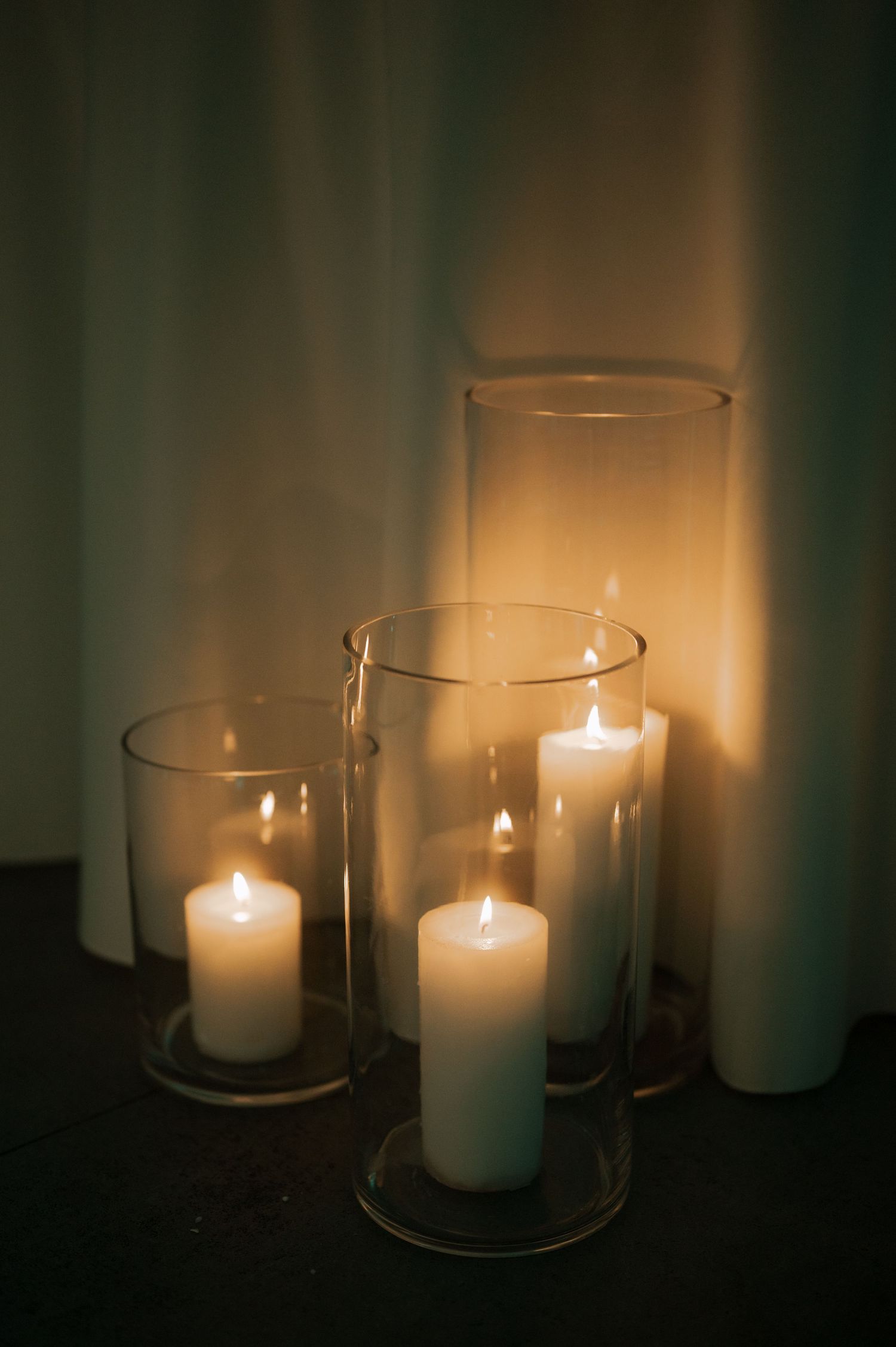 A series of glowing white candles in glass holders cast a warm, atmospheric light against a dark background.