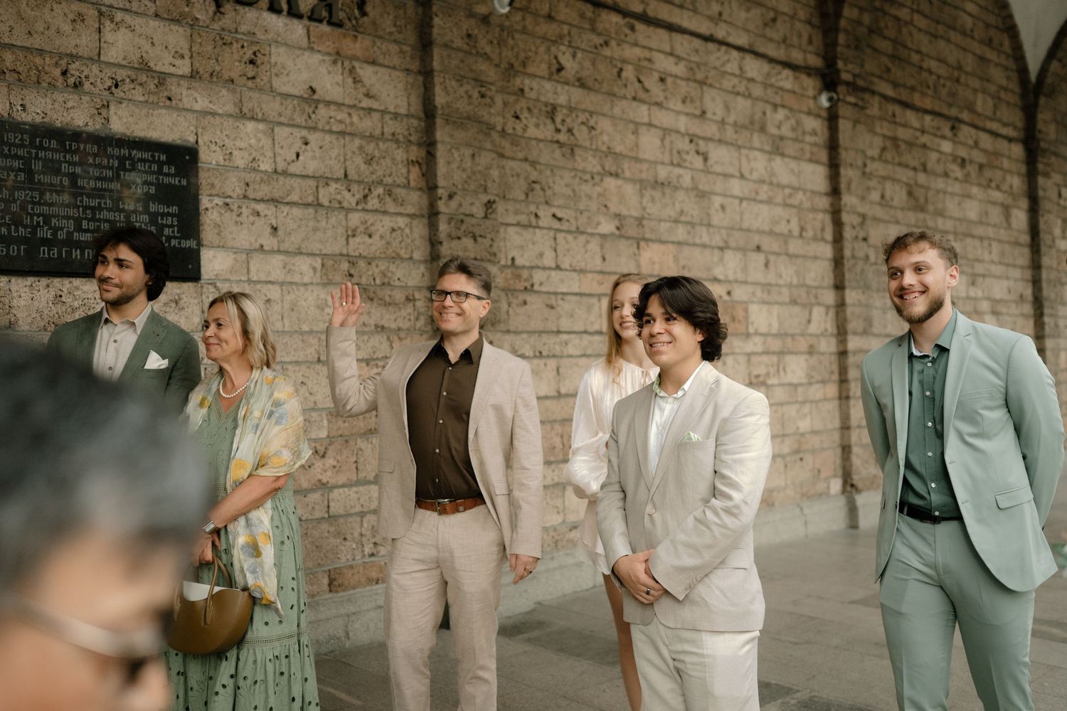 Wedding party members in coordinated mint green and white attire pose against a rustic brick wall.