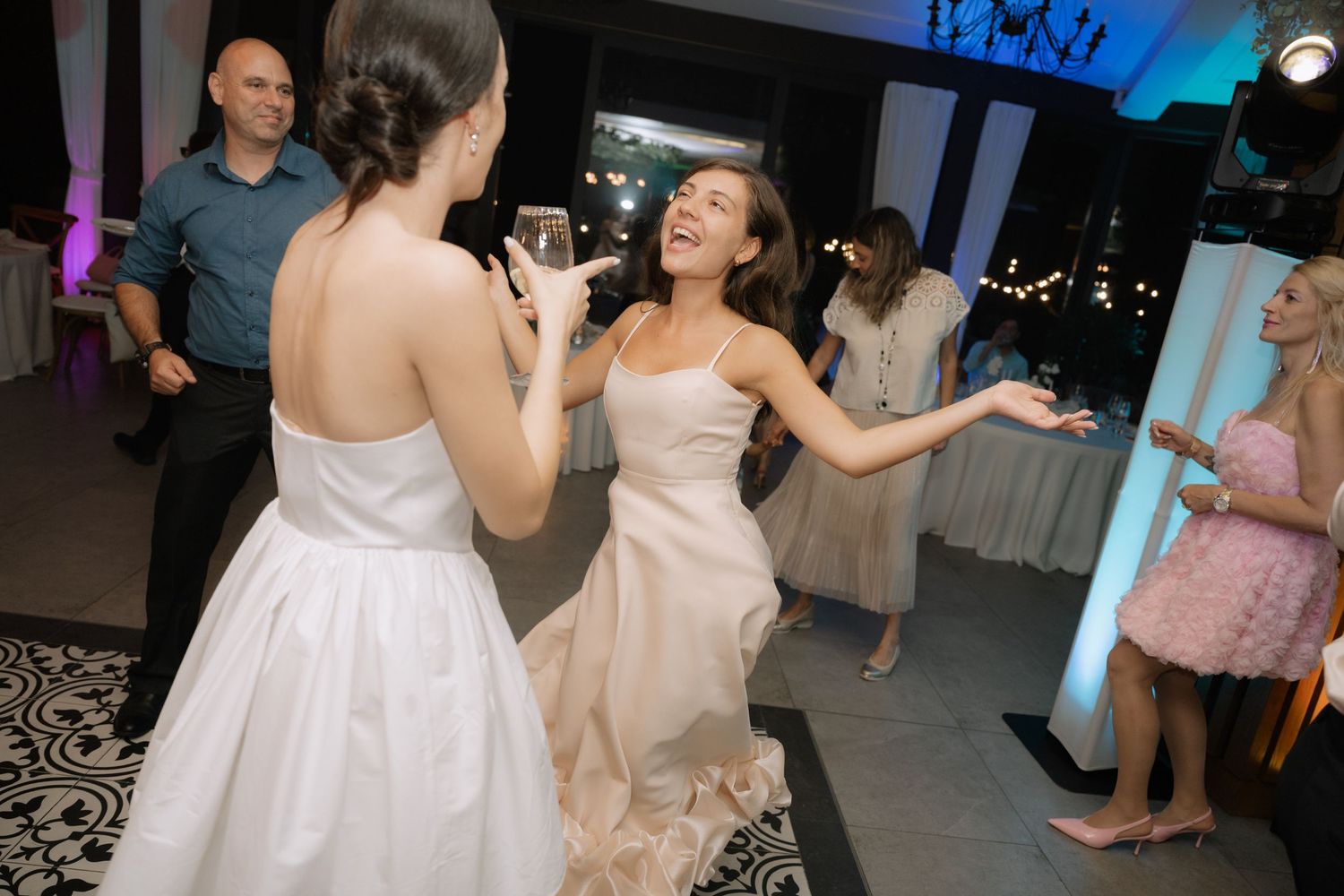 Wedding guests dance together on a dimly lit dance floor at an evening reception celebration.