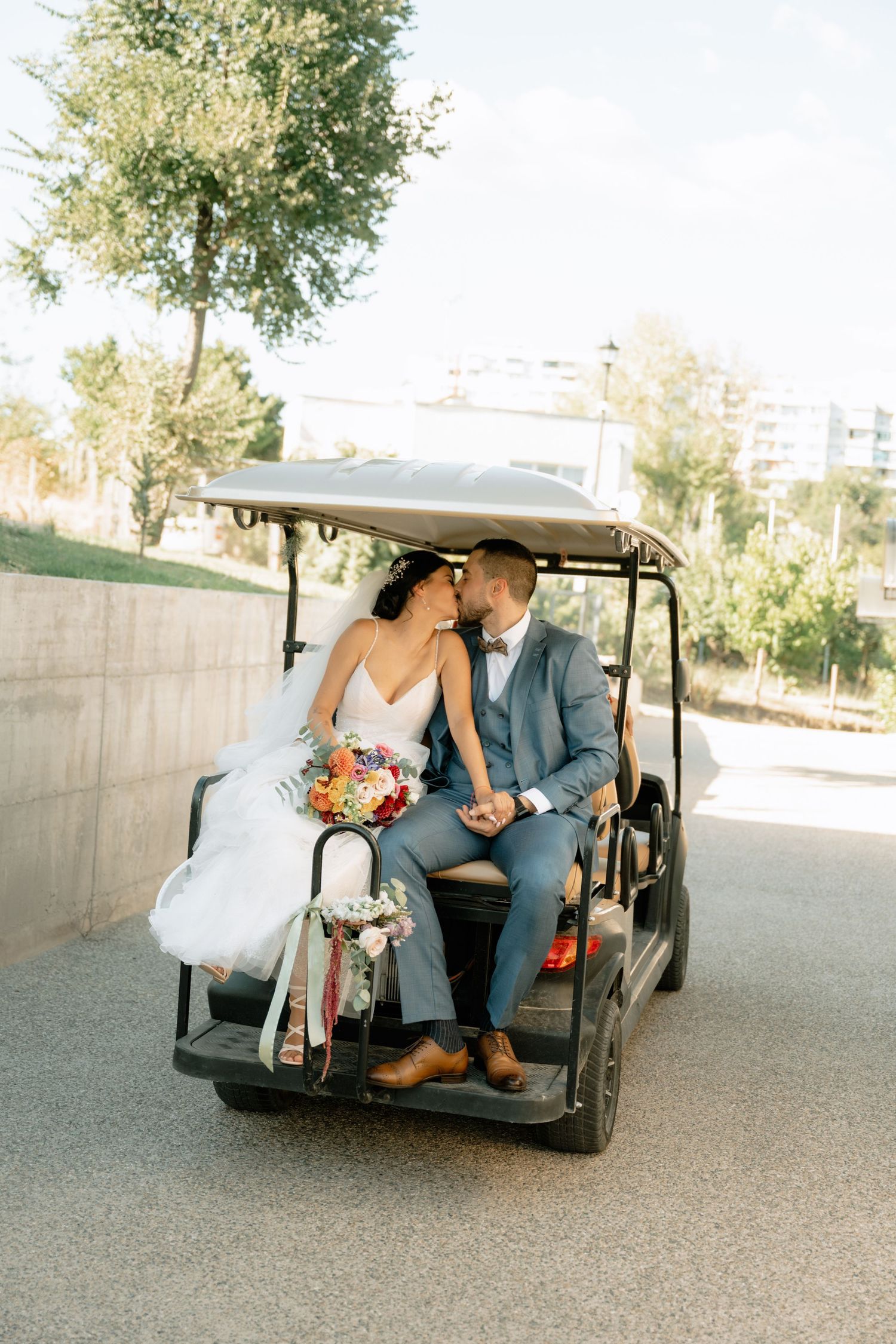 A romantic couple in wedding attire share an intimate moment while seated in a golf cart on their special day.