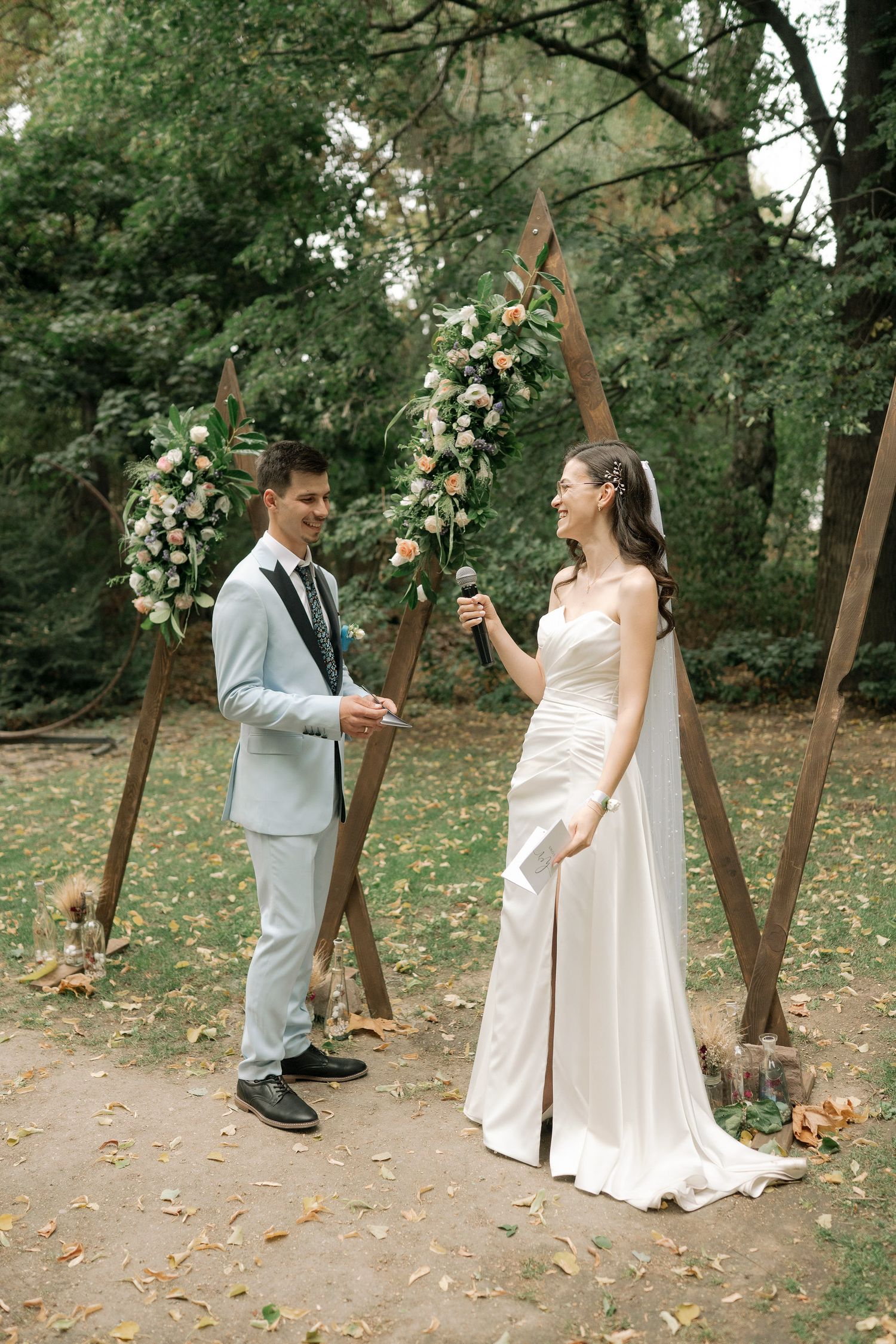 A bride and groom share a playful dance moment in a wooded outdoor setting surrounded by fallen autumn leaves.