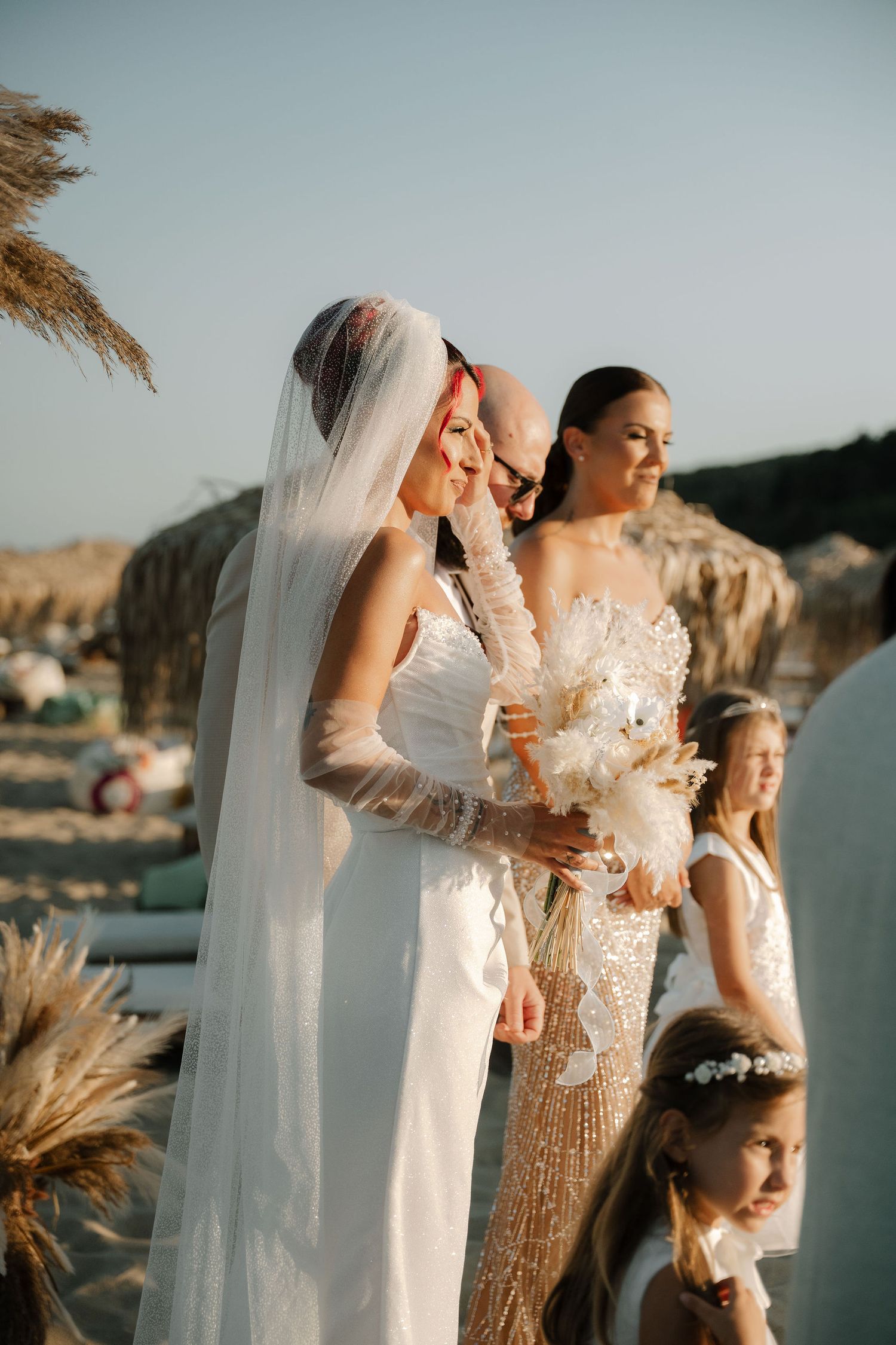 Wedding party stands together in golden sunlight by the water with pampas grass swaying in the breeze.