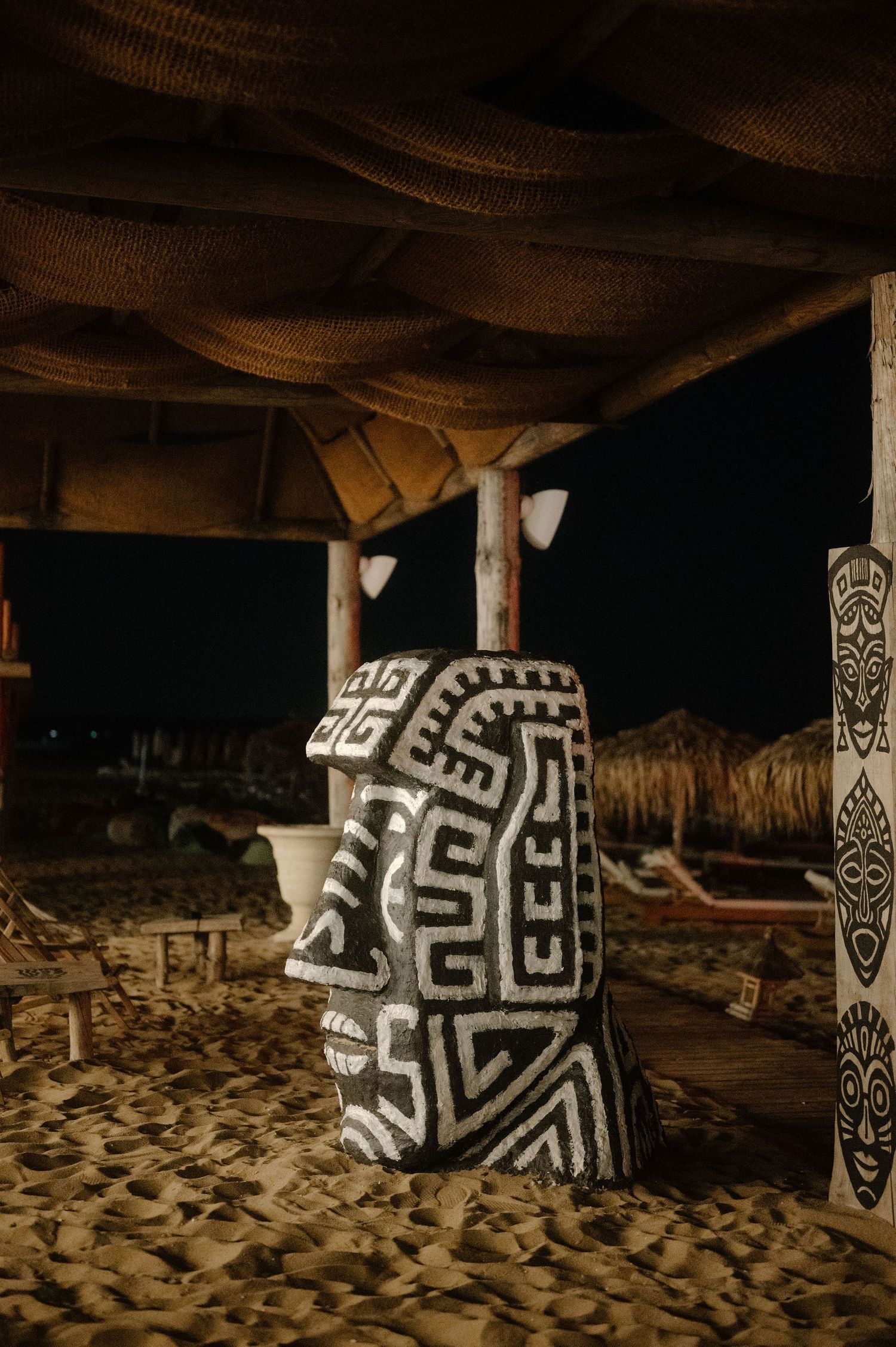 Abstract black and white geometric patterns painted on stone pillars in a dark sandy environment create a tribal atmosphere.