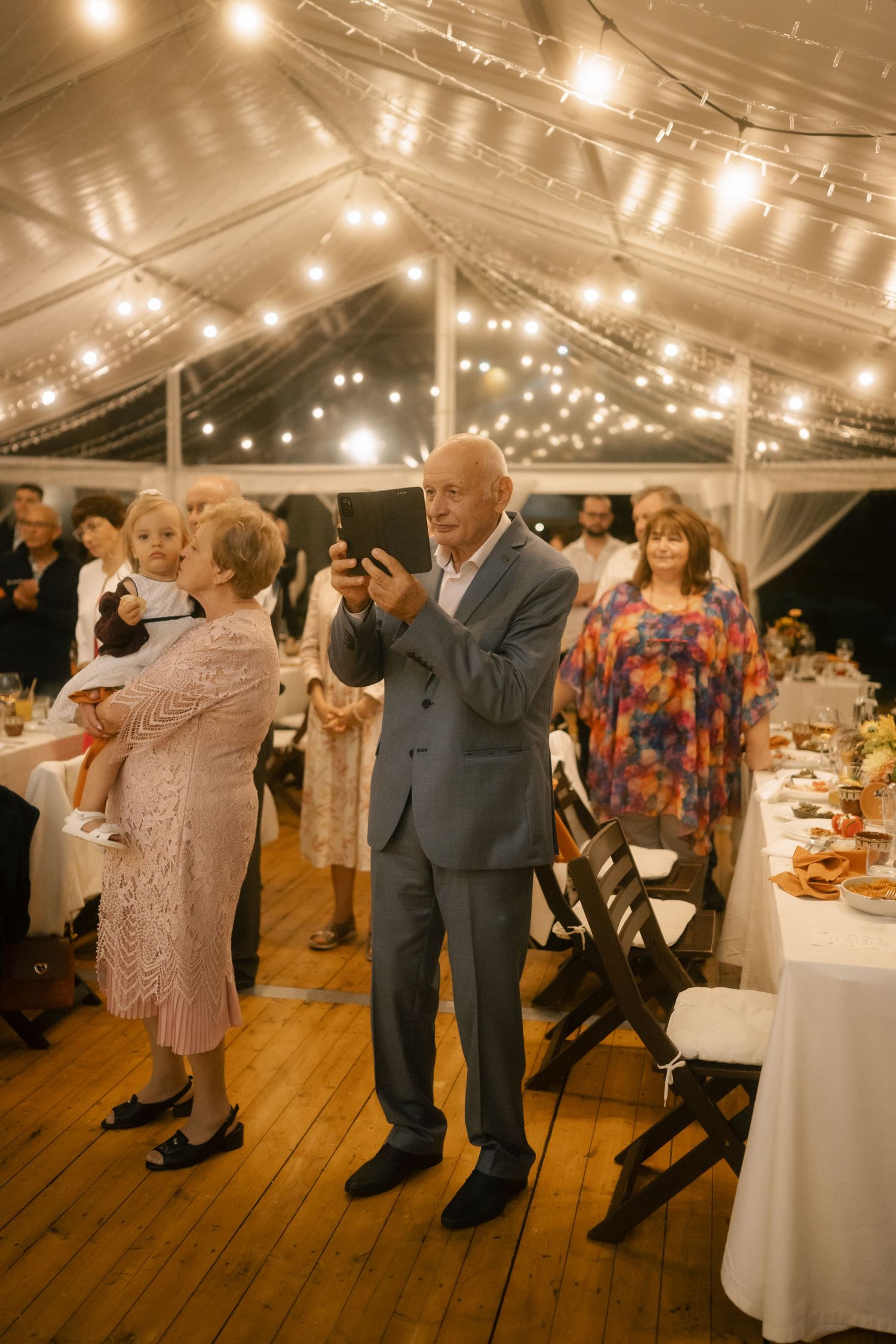 Party guests enjoying a lively dance celebration in an illuminated tent venue with round tables.
