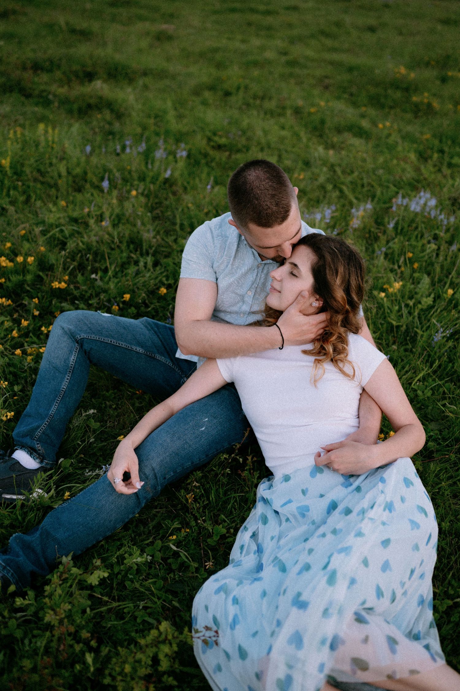 A couple embraces while sitting in a flowering meadow at dusk.